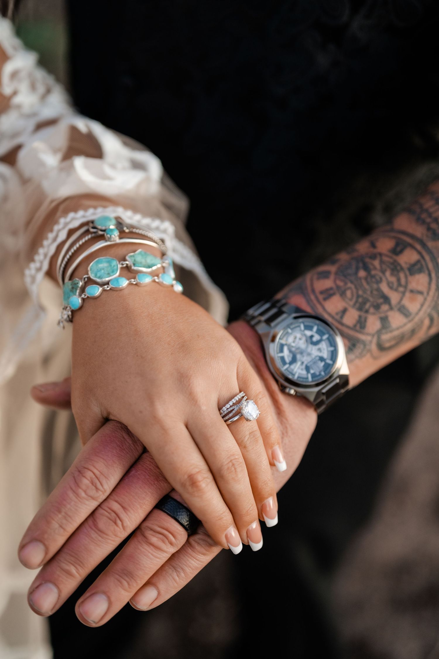 Close-up of hands wearing turquoise jewelry and tattoos resting together in an intimate moment.