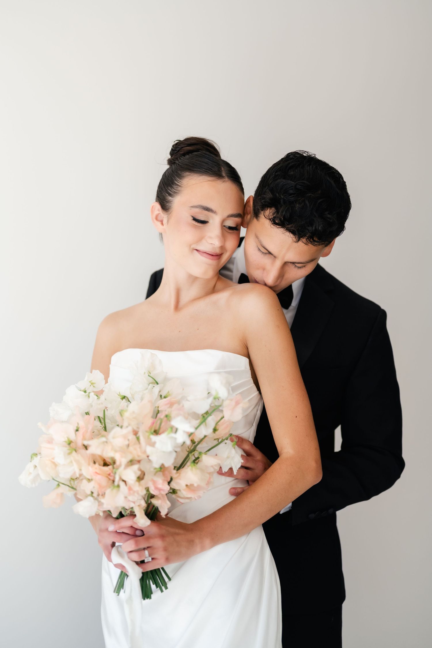 Romantic wedding couple embraces while bride holds a soft pink and white floral bouquet. Moments on Main Photographer.