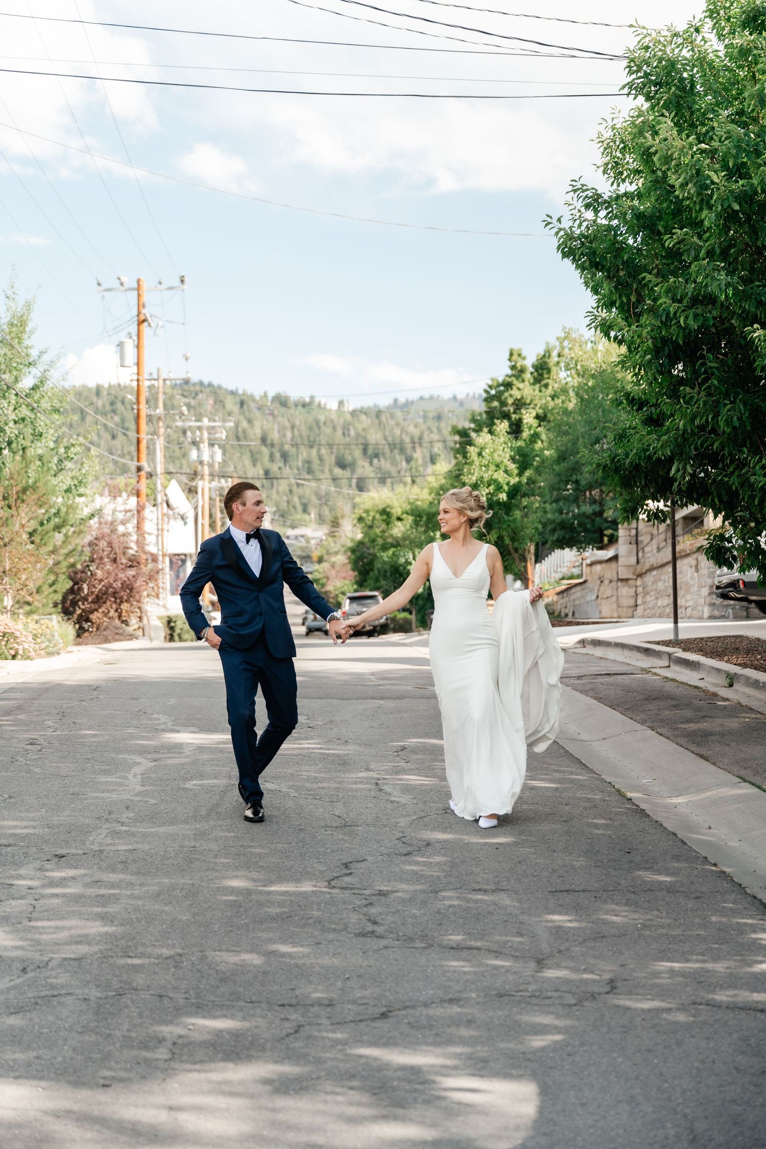 Bride and groom holding hands walking down a sunny street in a white dress and navy suit just outside the Washington School House Hotel.