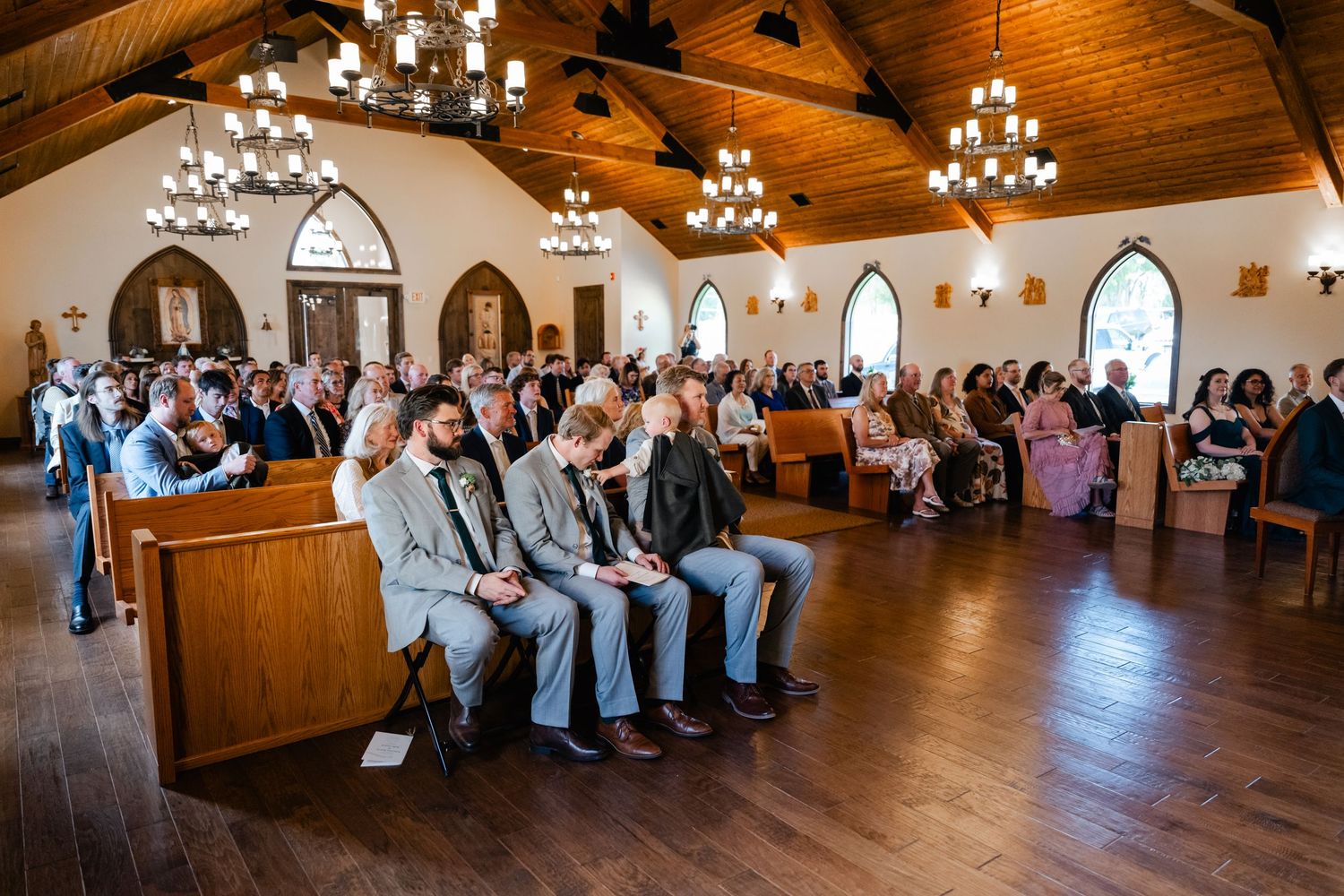 A panoramic view of a church interior with wooden beams and chandeliers.