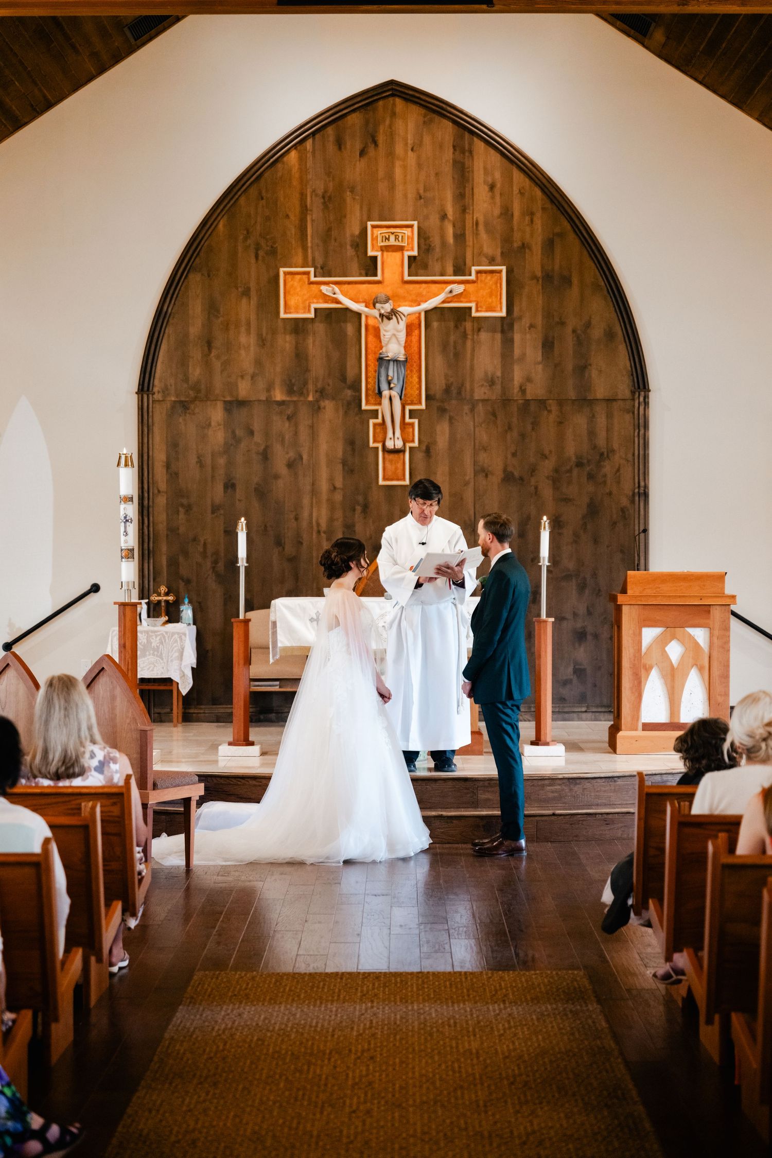 A church sanctuary with wooden walls features a crucifix and white wedding decorations.