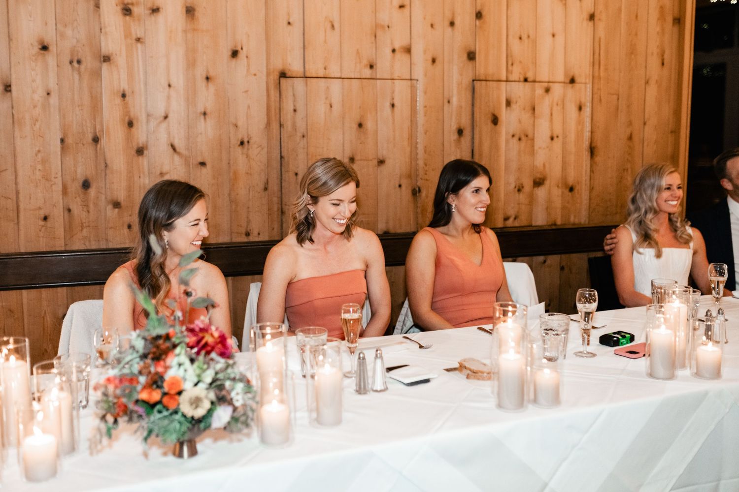Long wooden reception table set with candles and floral centerpieces in rustic barn venue.