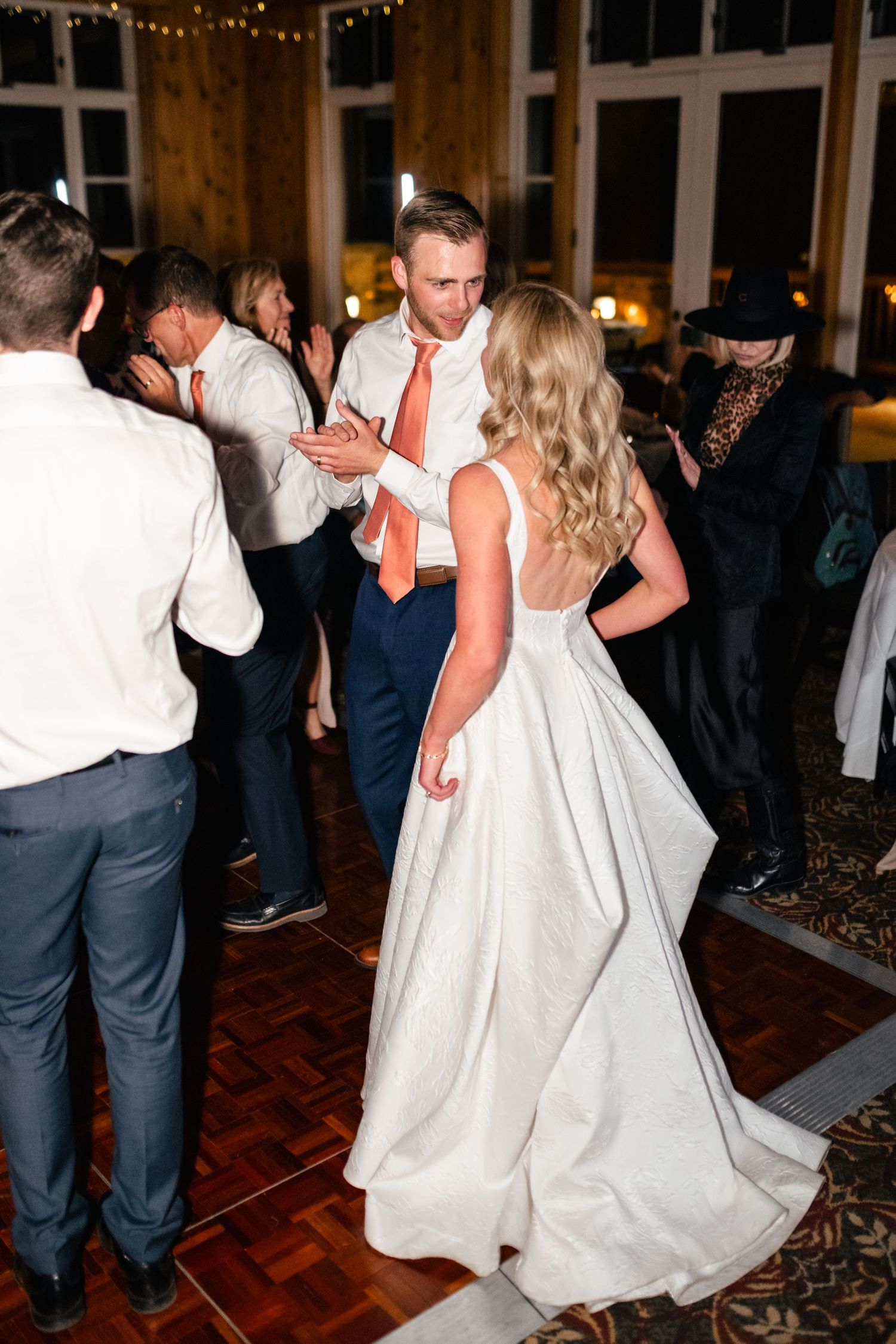 Wedding celebration with dancing couples on a parquet floor in an elegantly lit venue.