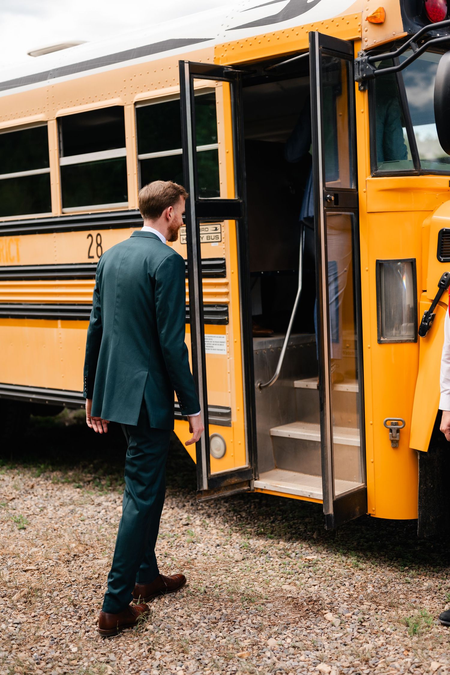 Yellow school bus parked on gravel with formal wedding party boarding.