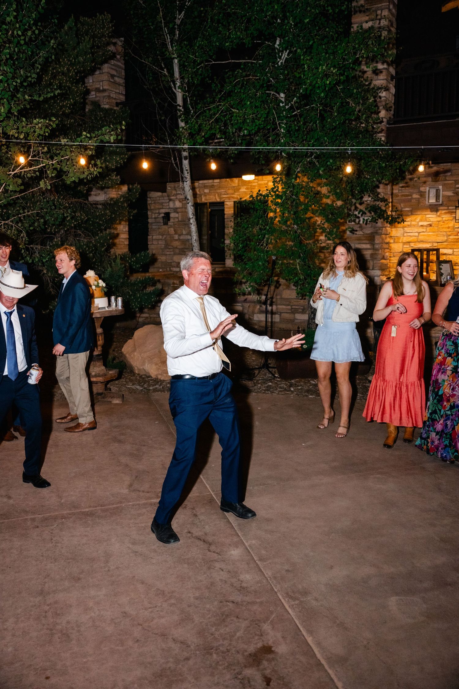 Wedding guest shows off dance moves on outdoor patio with string lights overhead.