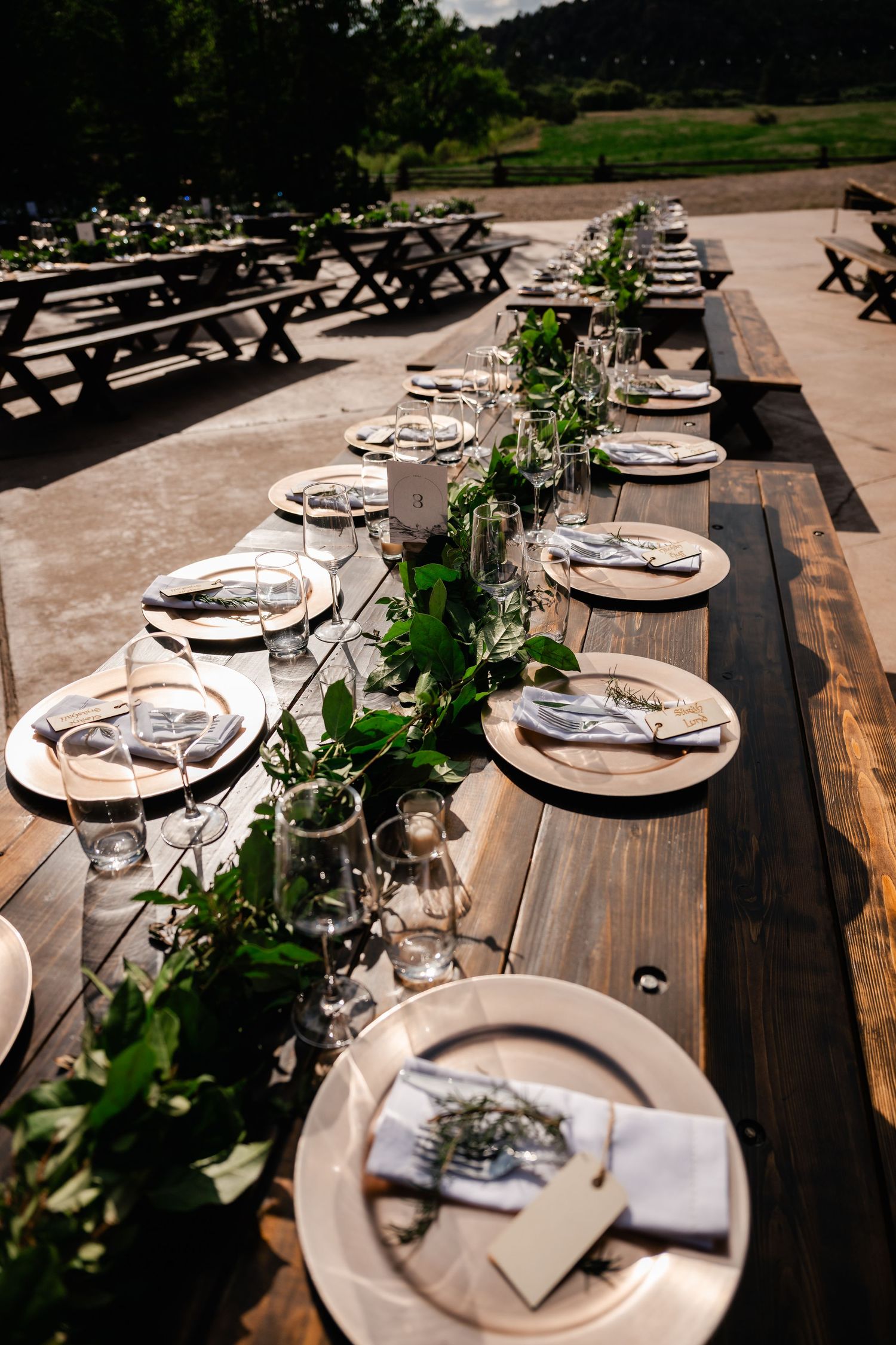 Rustic wooden tables set for a wedding reception with elegant place settings and natural greenery decor.