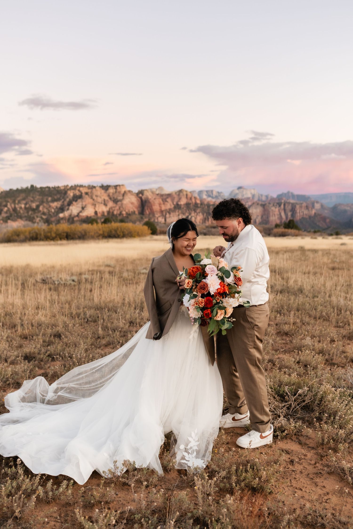 Wedding couple dances together in rustic field with mountain backdrop during golden hour.