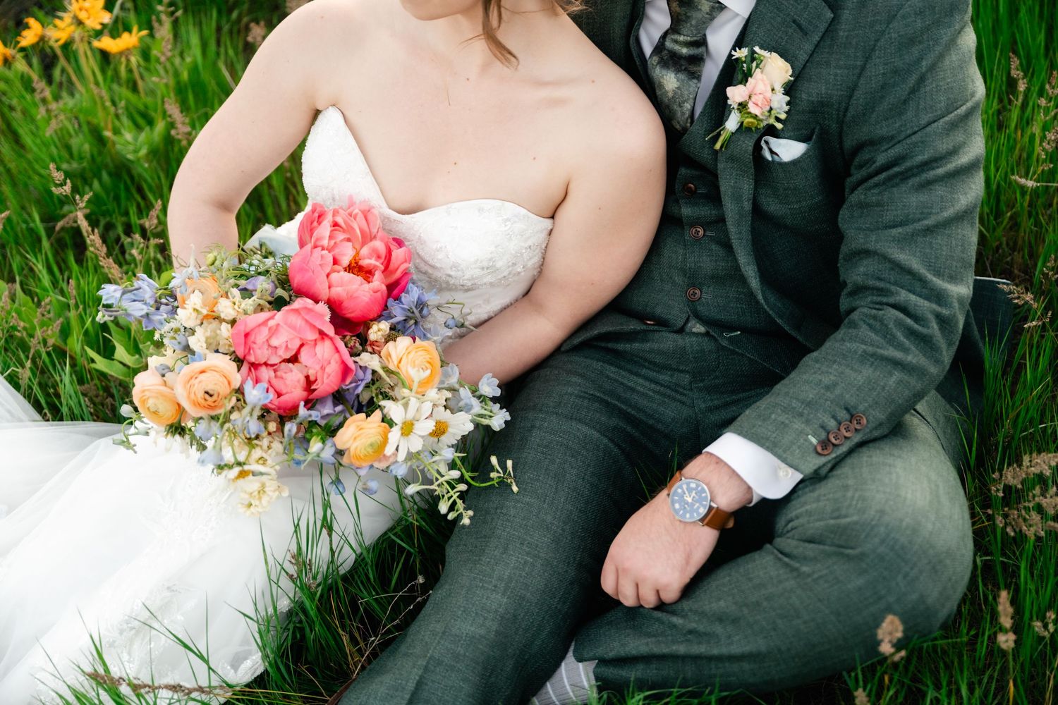 Couple sitting in lush grass holding colorful bouquets of spring flowers during an outdoor photo session.