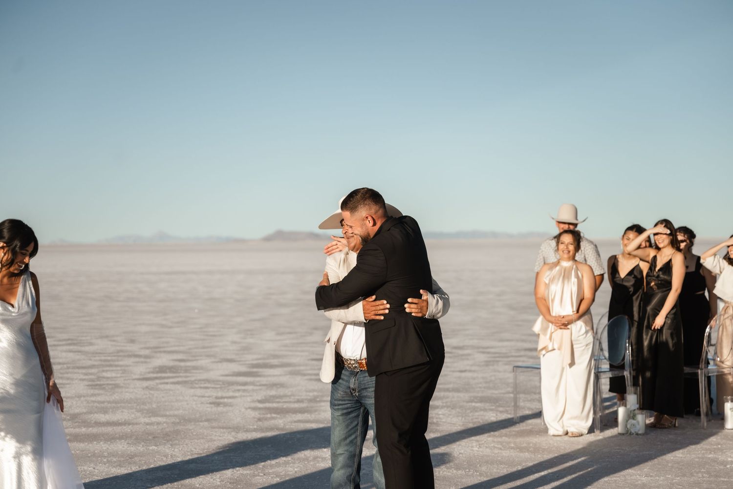 Wedding party gathered on salt flats for group photos with mountain backdrop.