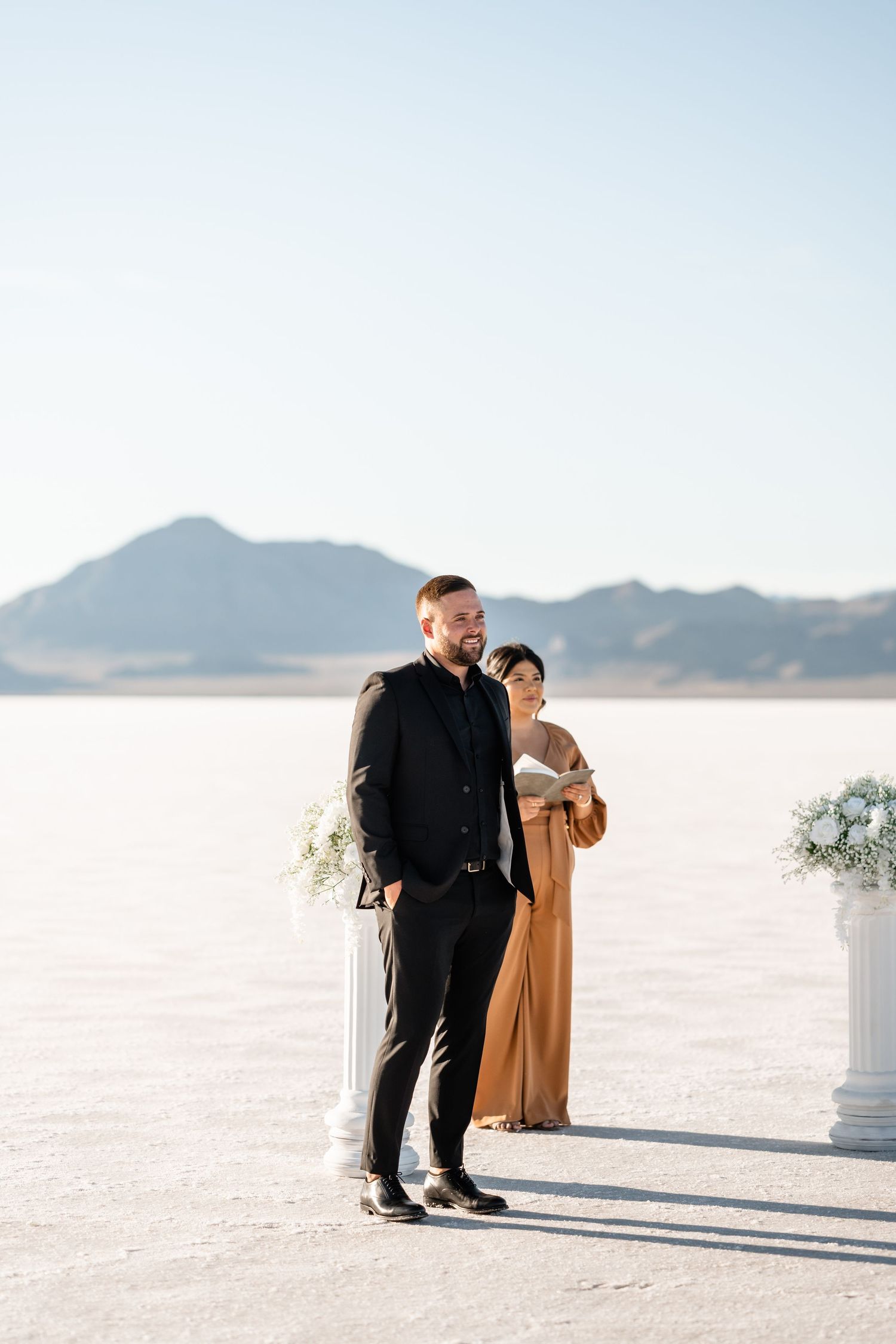 Wedding couple posing on salt flats with mountains in background during sunset.