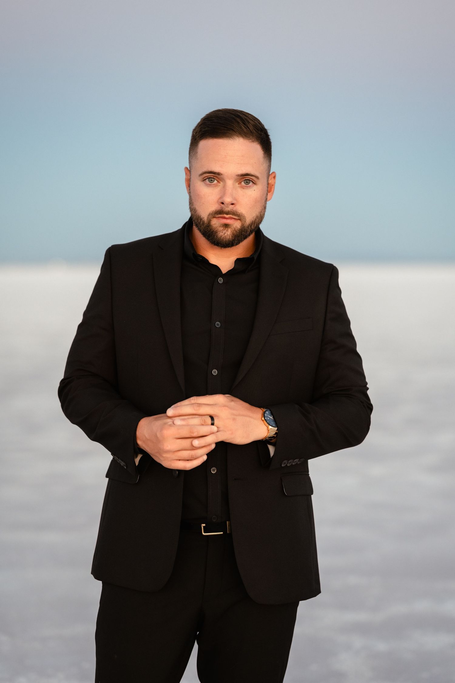 Professional portrait series of a man in a black suit against a cloudy sky background.
