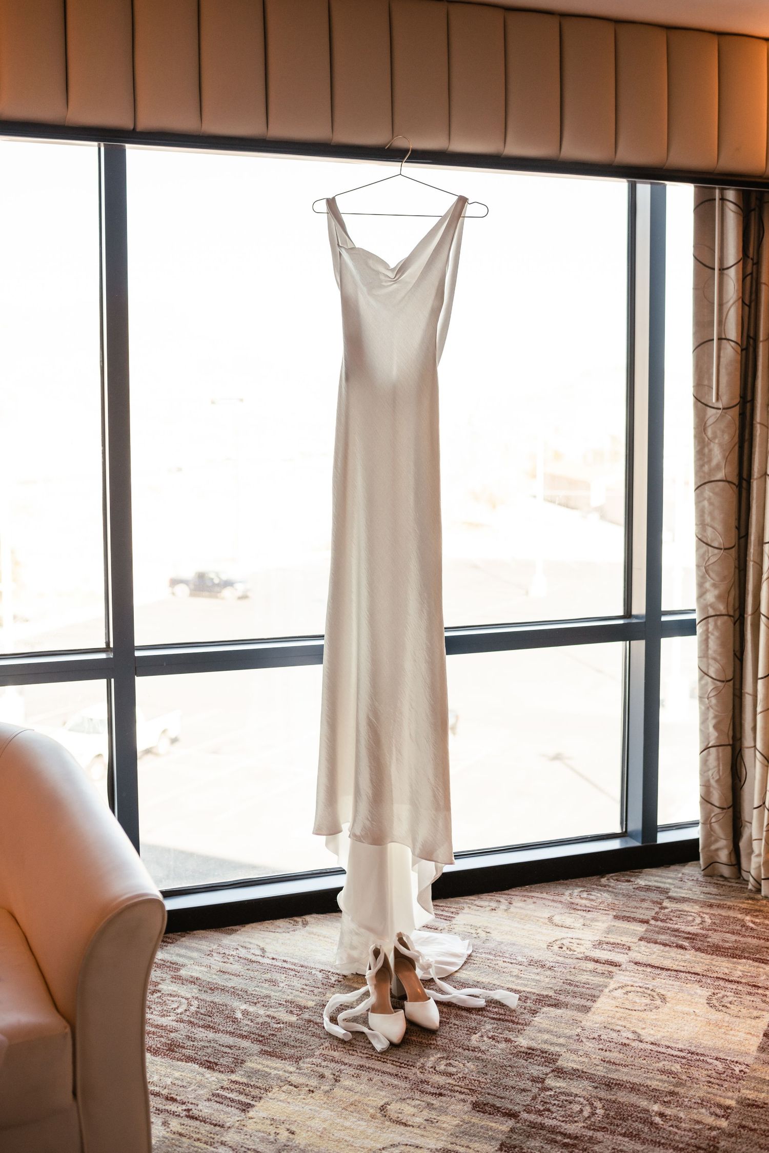 White wedding dress hanging in front of large windows with natural light streaming in.