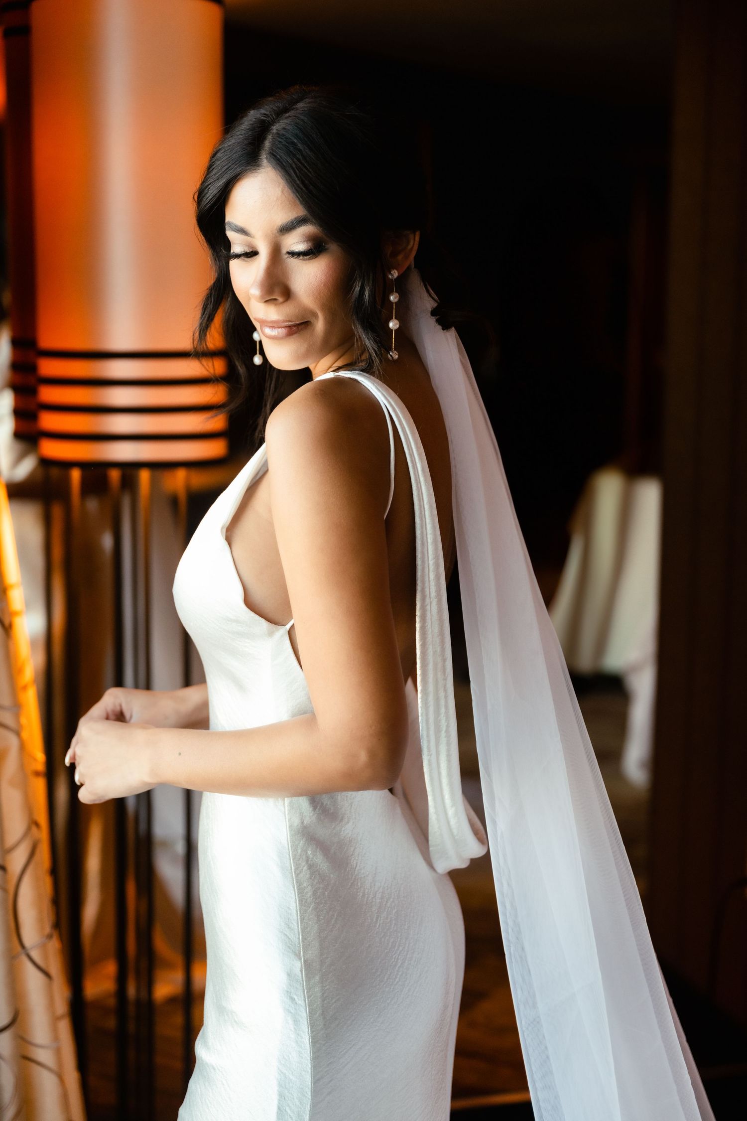 Bride in white dress preparing for wedding ceremony in dimly lit room.