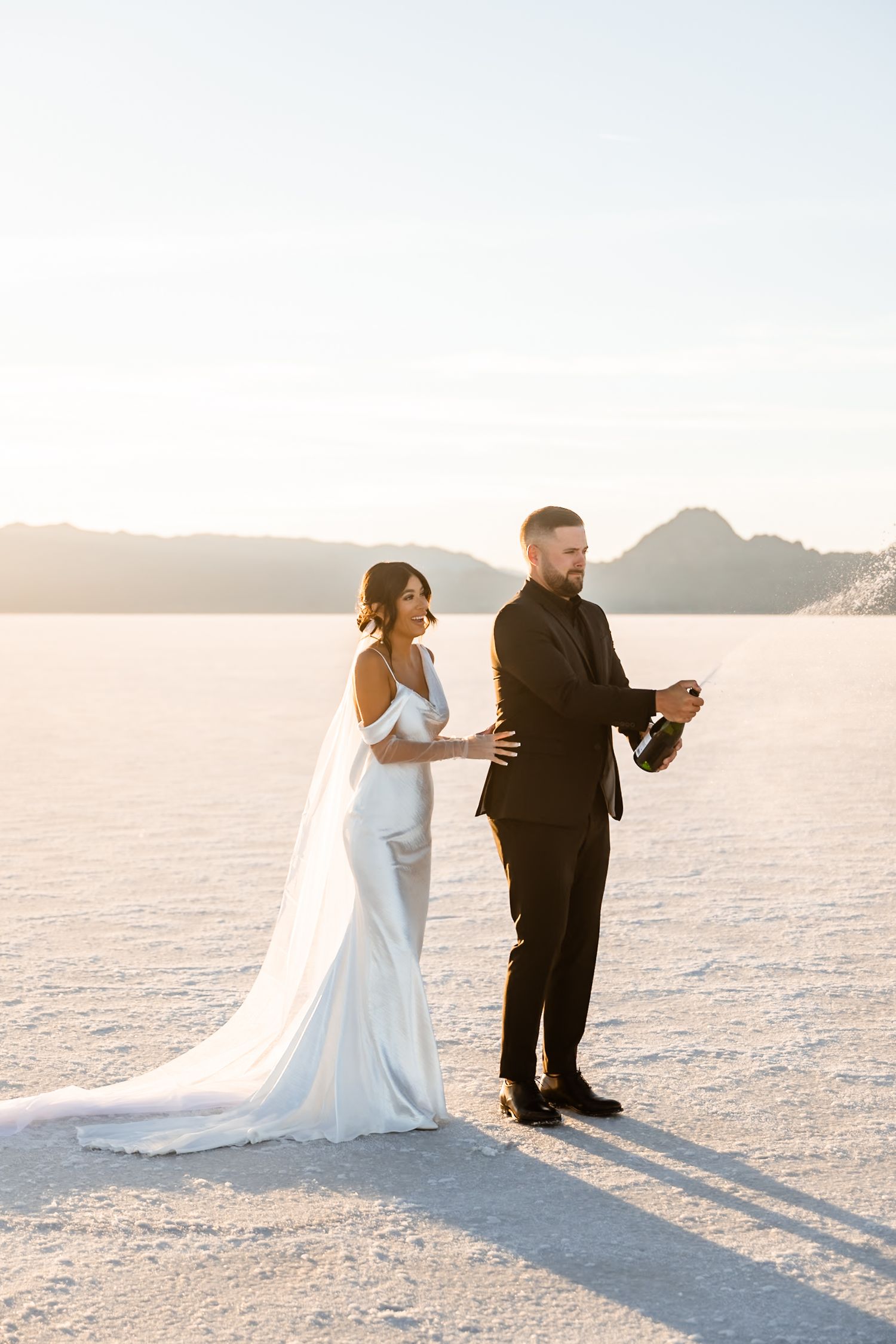 Newlyweds share playful moments on vast white salt flats during sunset photo session.