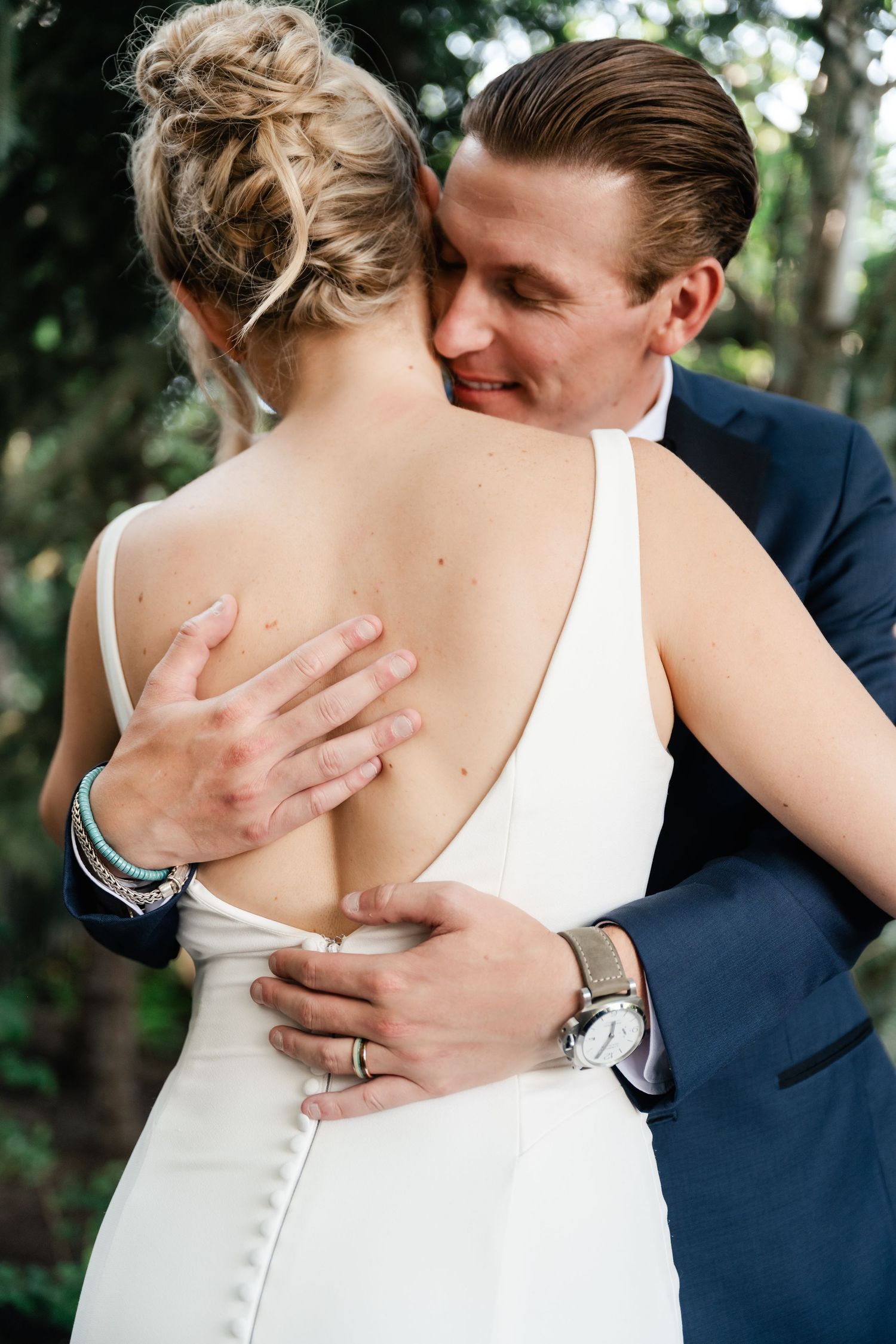 Close-up detail shots of tender embrace between newlyweds showing wedding dress buttons and ring.