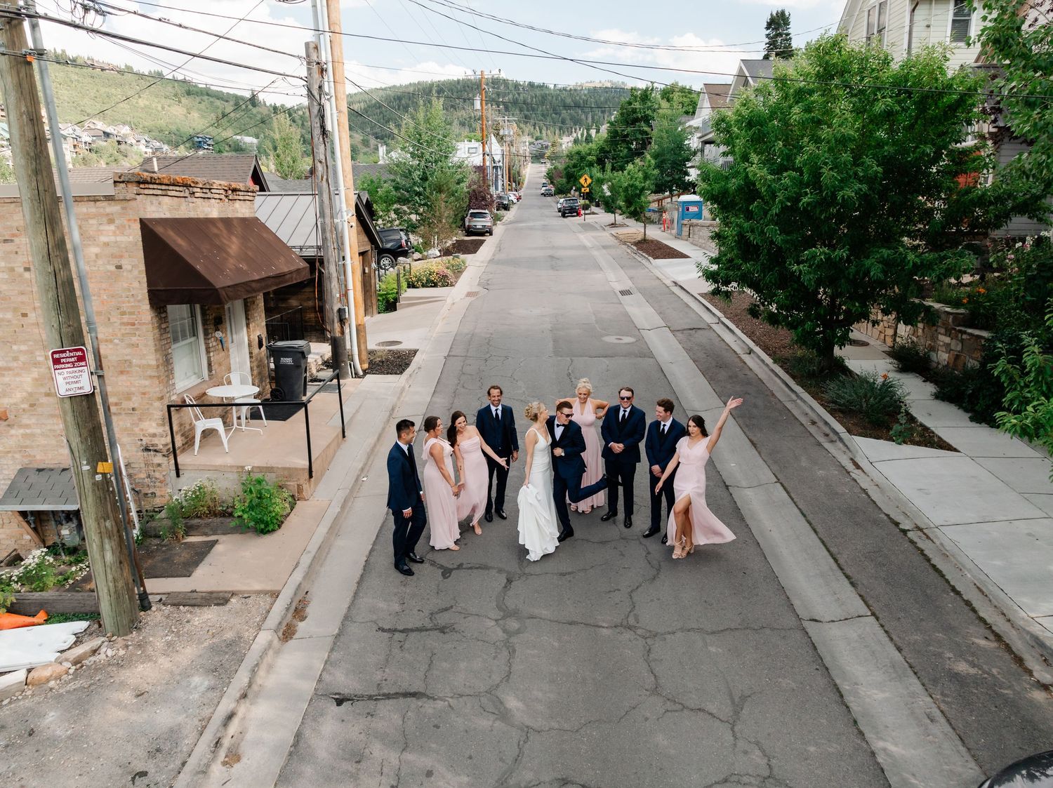 Bridal party walking down a steep residential street lined with power lines and trees.