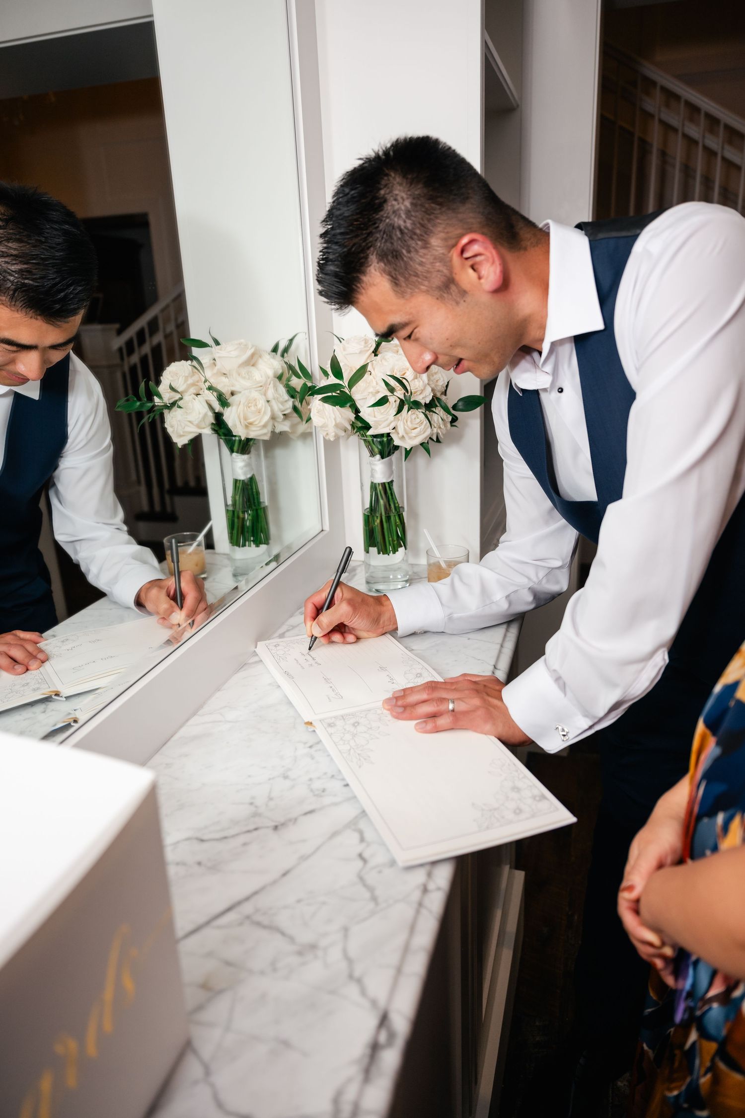 Wedding party members sign documents on a marble counter.