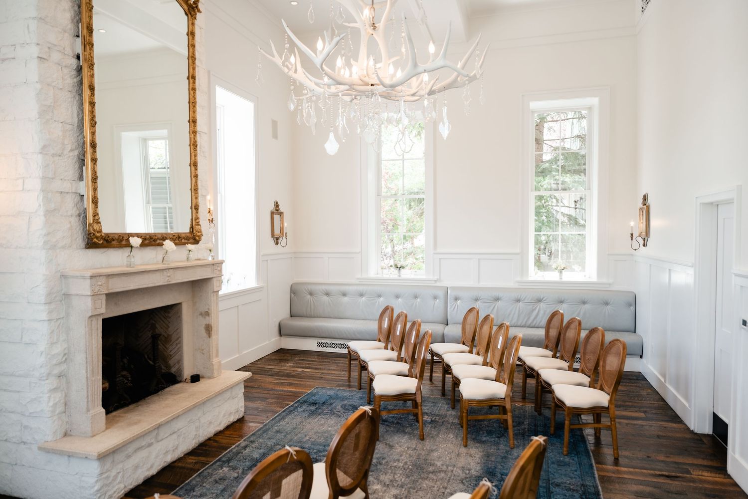Elegant white dining room interior with rustic wooden floors, white walls, and antique gold wall sconces.
