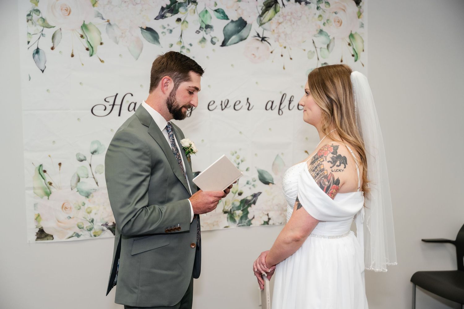 A couple shares a tender moment in front of a floral wall during their wedding celebration.