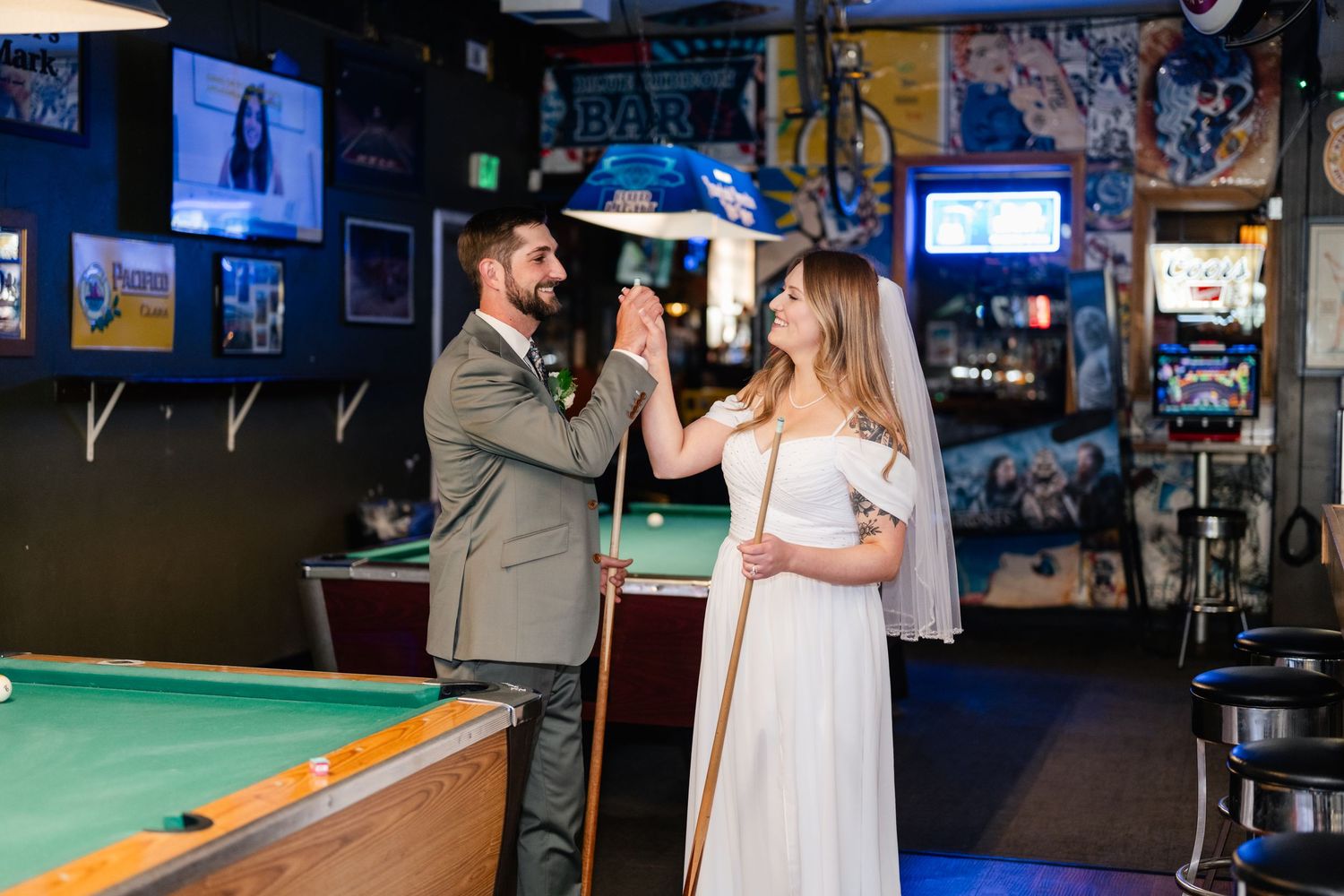 A couple in wedding attire shares an intimate moment near a pool table in a bar setting.