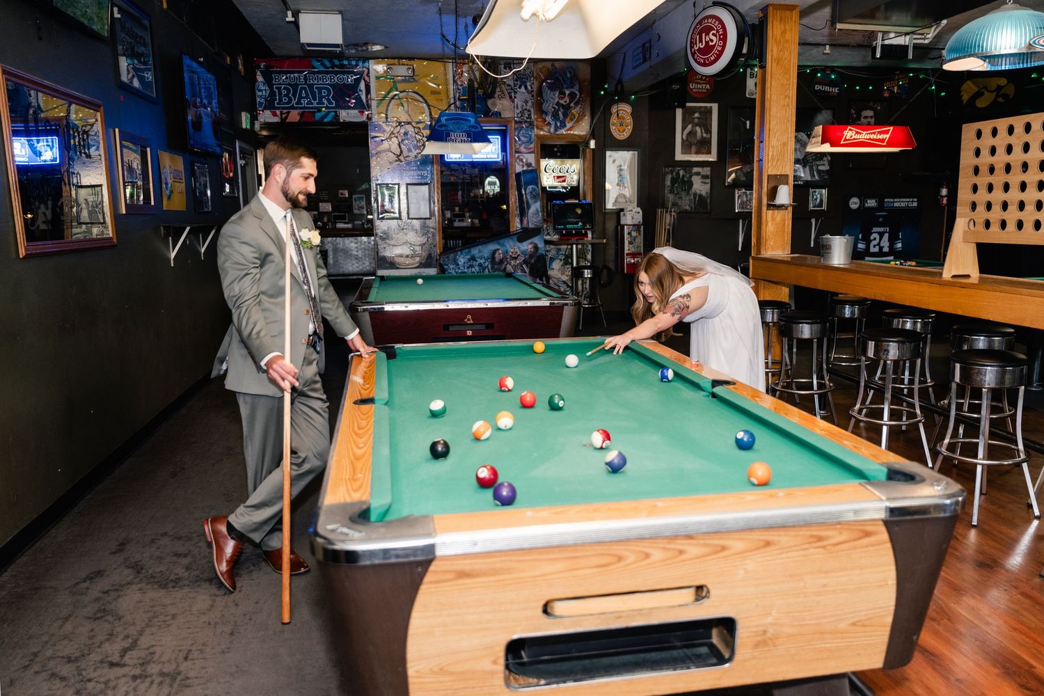 A couple playing pool together at a dimly lit bar with neon signs and bar decor in the background.