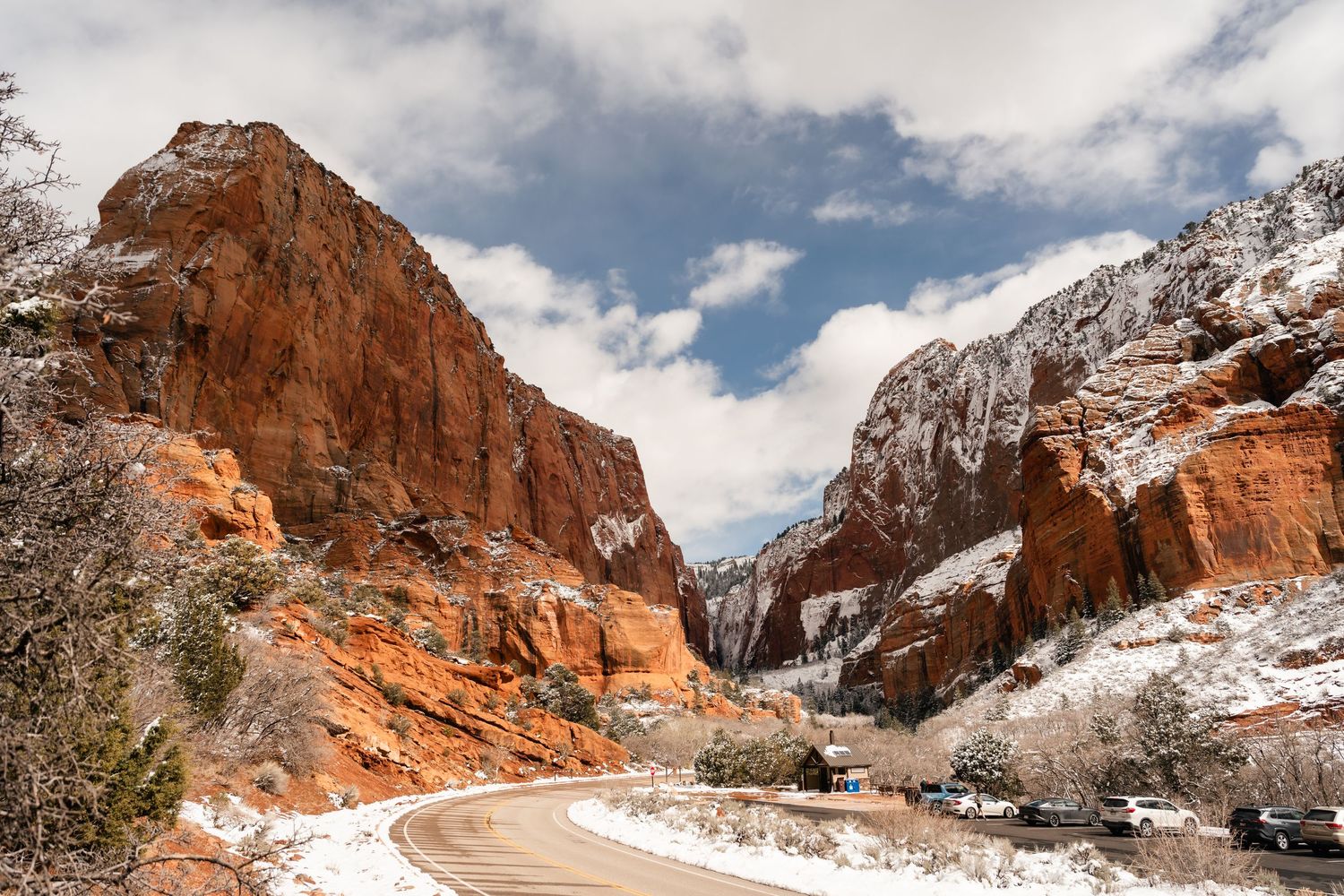 A panoramic winter view of red rock formations and winding roads in Zion National Park covered in fresh snow.