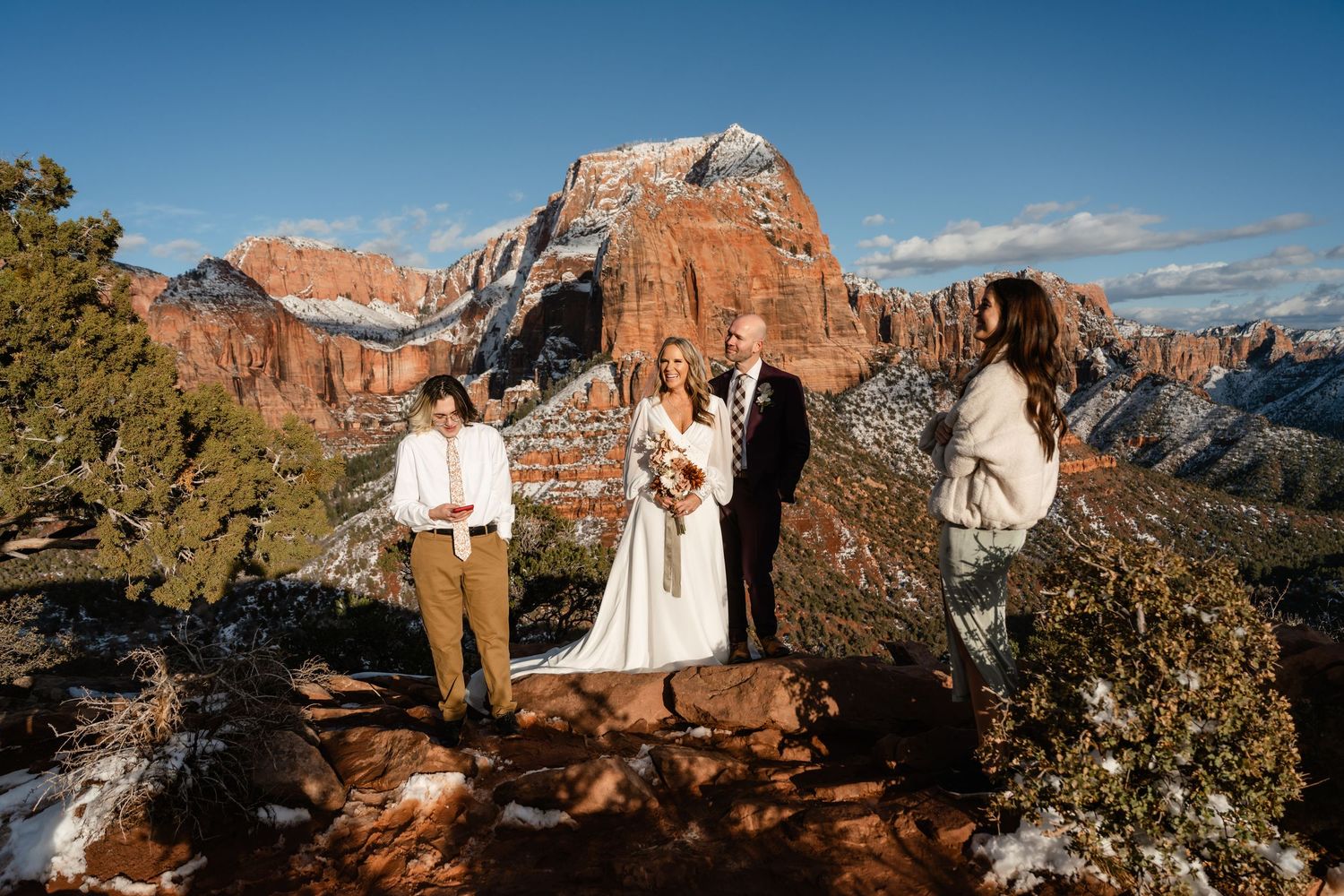 An intimate wedding ceremony takes place on a mountain overlook with red rock formations in the background.