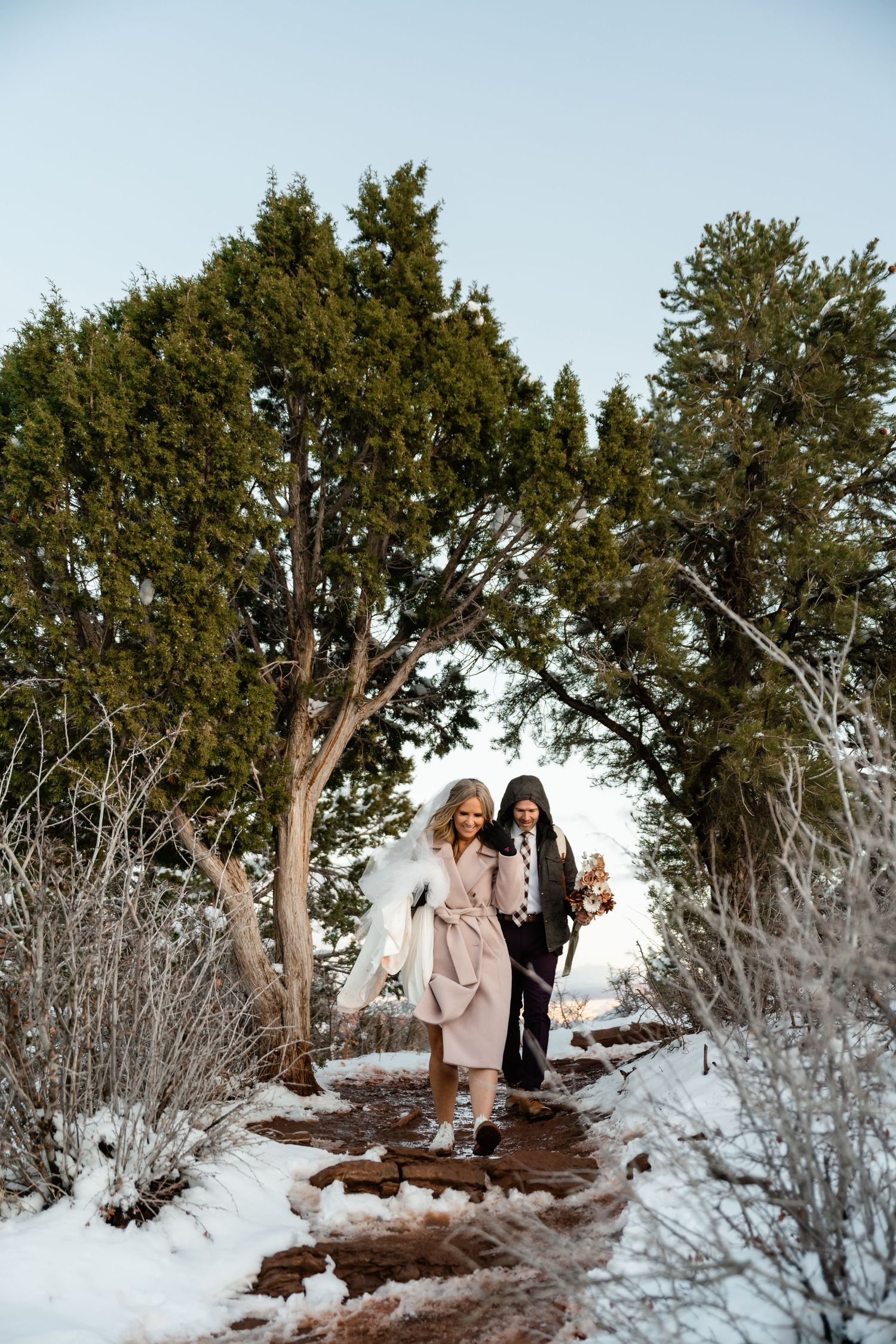 Snow-covered trail through evergreen trees and brush in a winter mountain landscape.