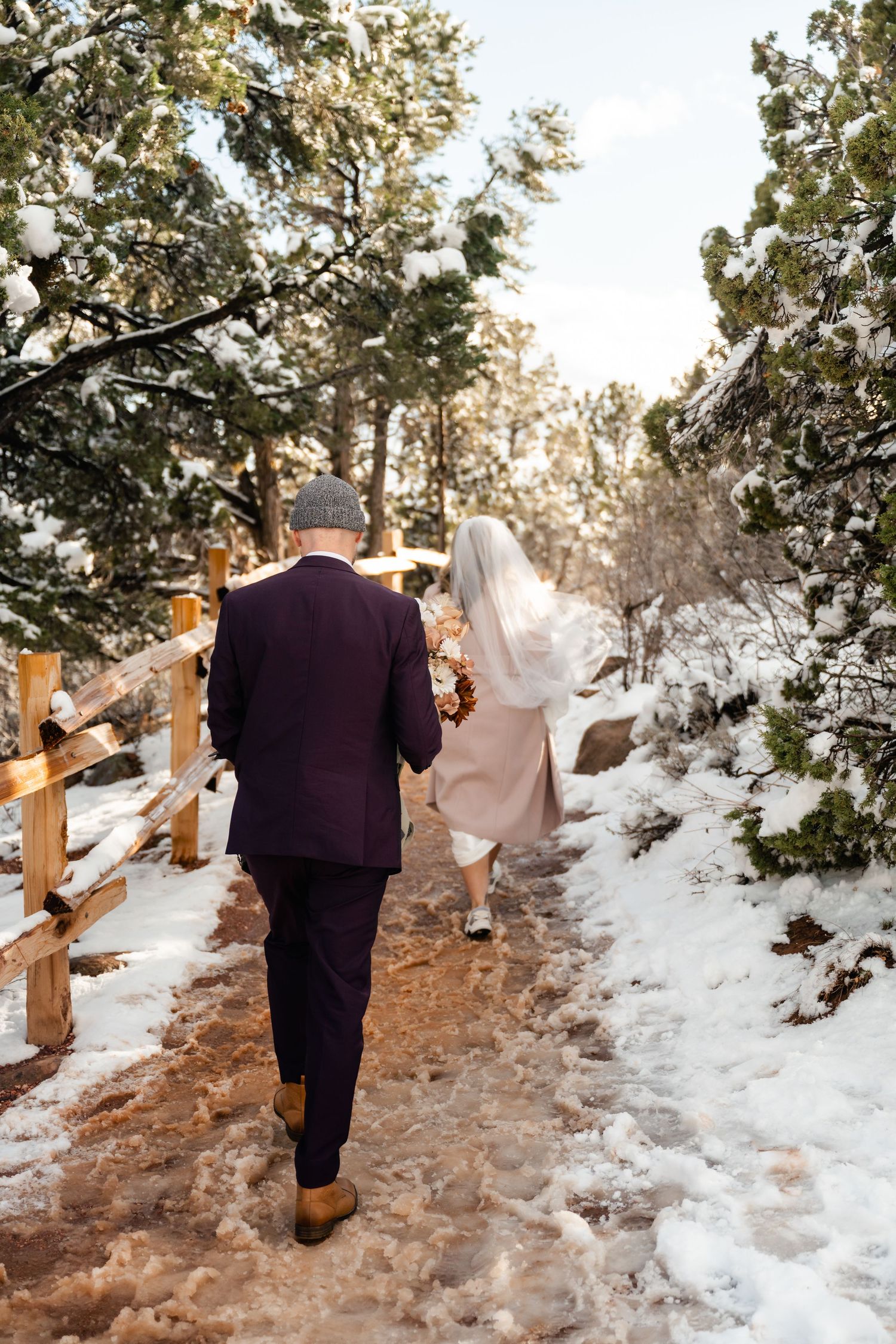People walking along a snowy trail with wooden railings through red rock terrain.