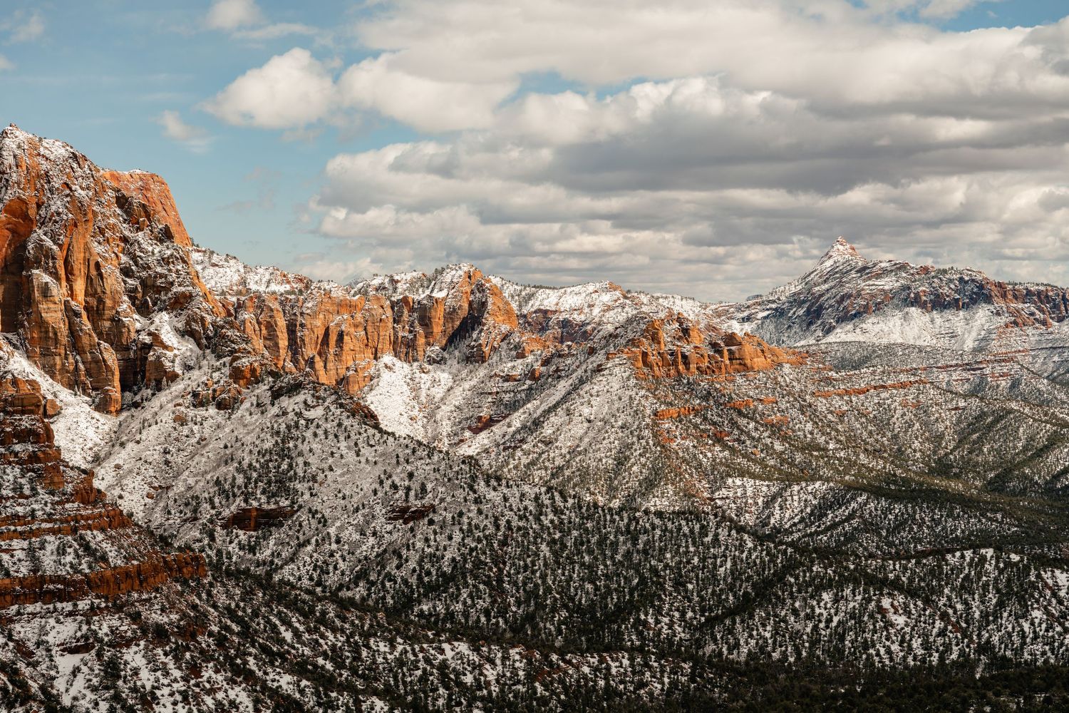Dramatic mountain landscape with snow-capped red rock formations stretching across the horizon.