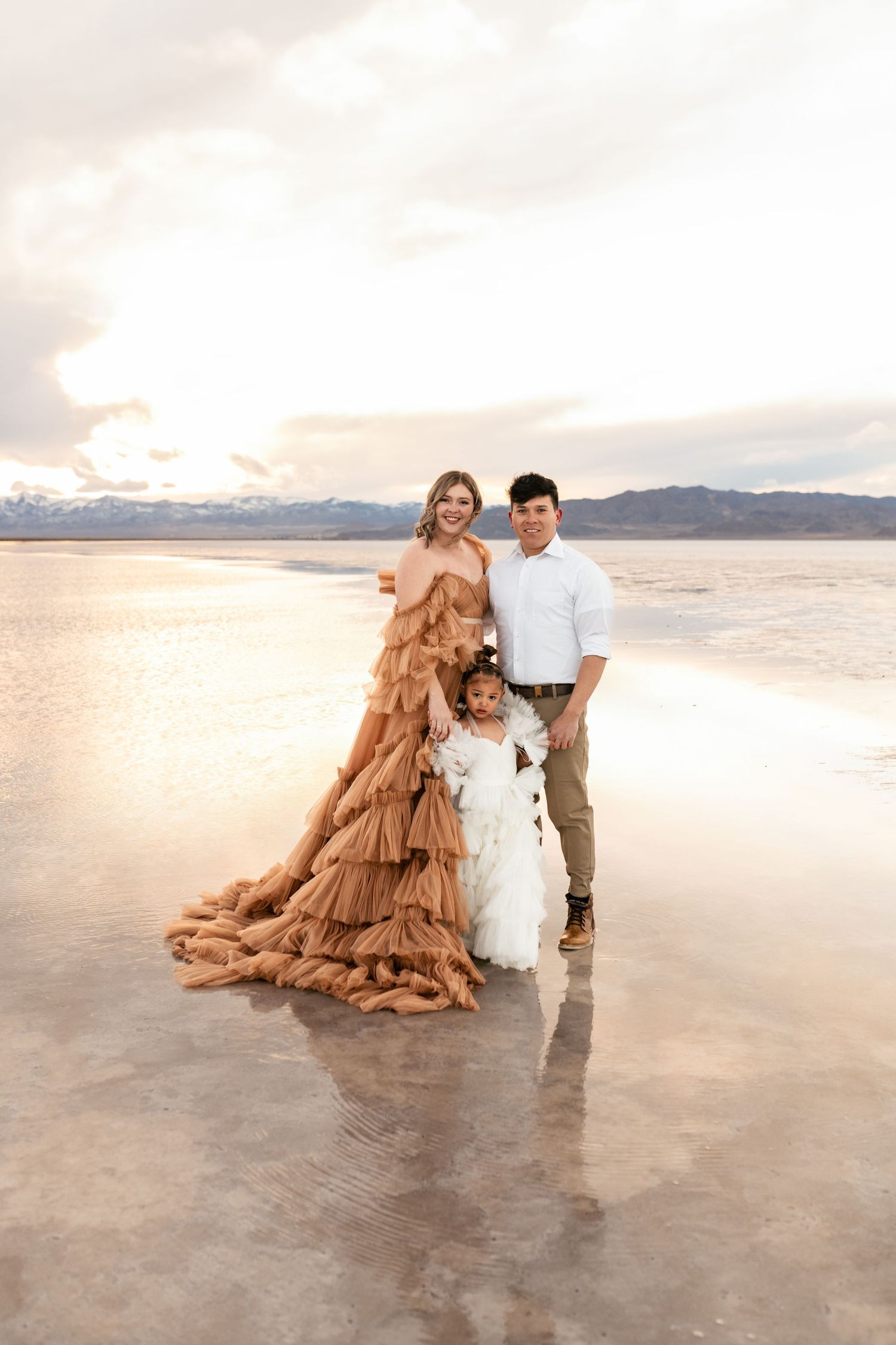 Utah Salt Flats PhotographerFamily portrait on reflective salt flats at sunset with mountains in background wearing elegant flowing dresses.