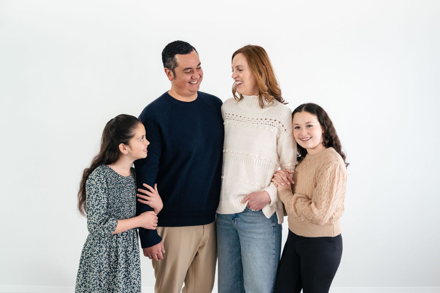 A group of four people wearing casual clothing laugh and smile together against a white background.