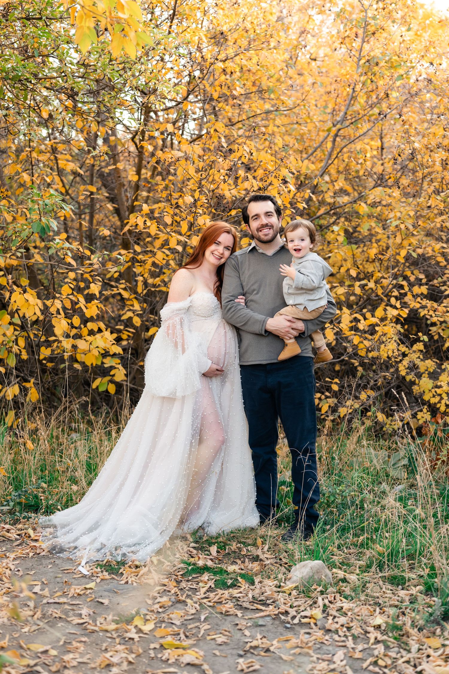 A family stands together on a path surrounded by vibrant yellow autumn foliage on a sunny fall day.