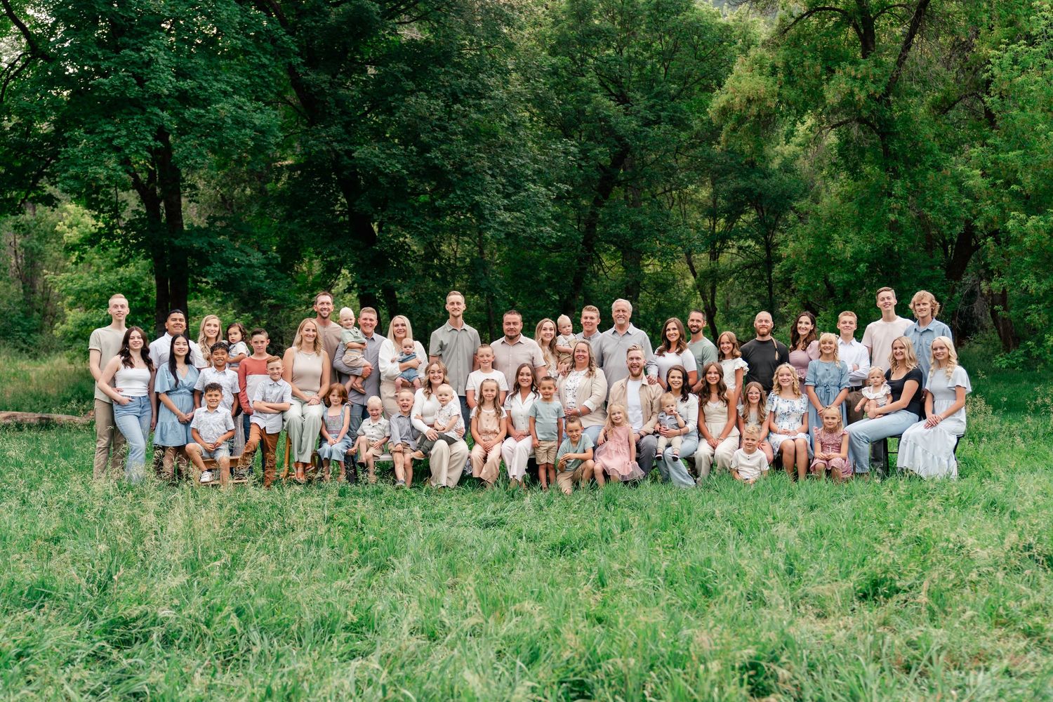 A large group of people in white and beige outfits pose together on a grassy hillside for outdoor portraits.