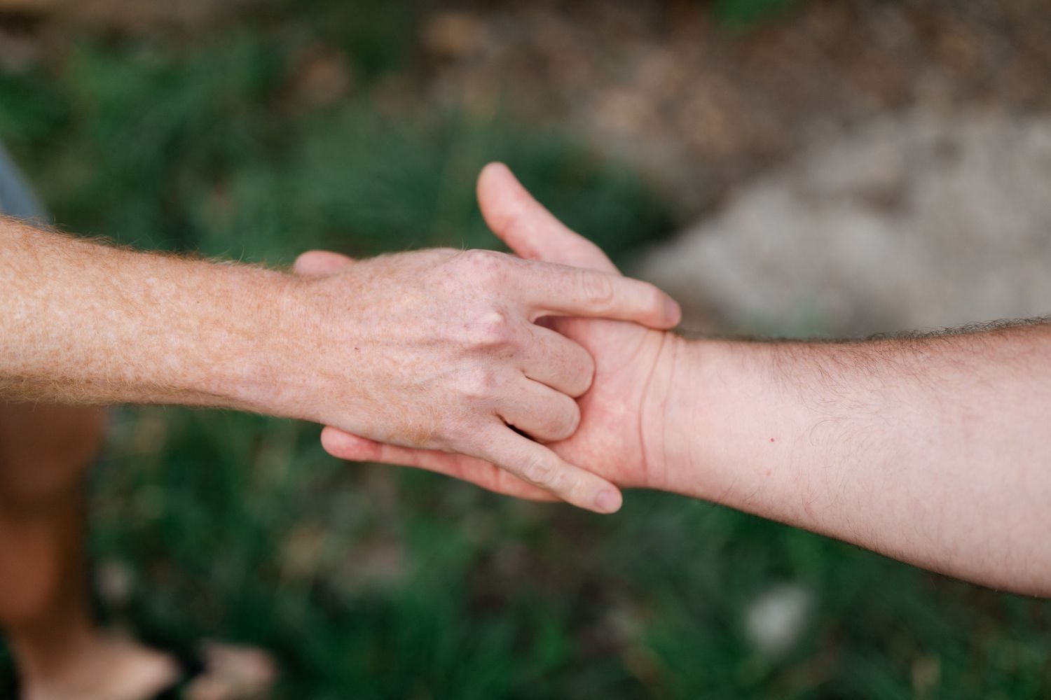 Two people holding hands outdoors with green grass in the background, symbolizing connection and support.