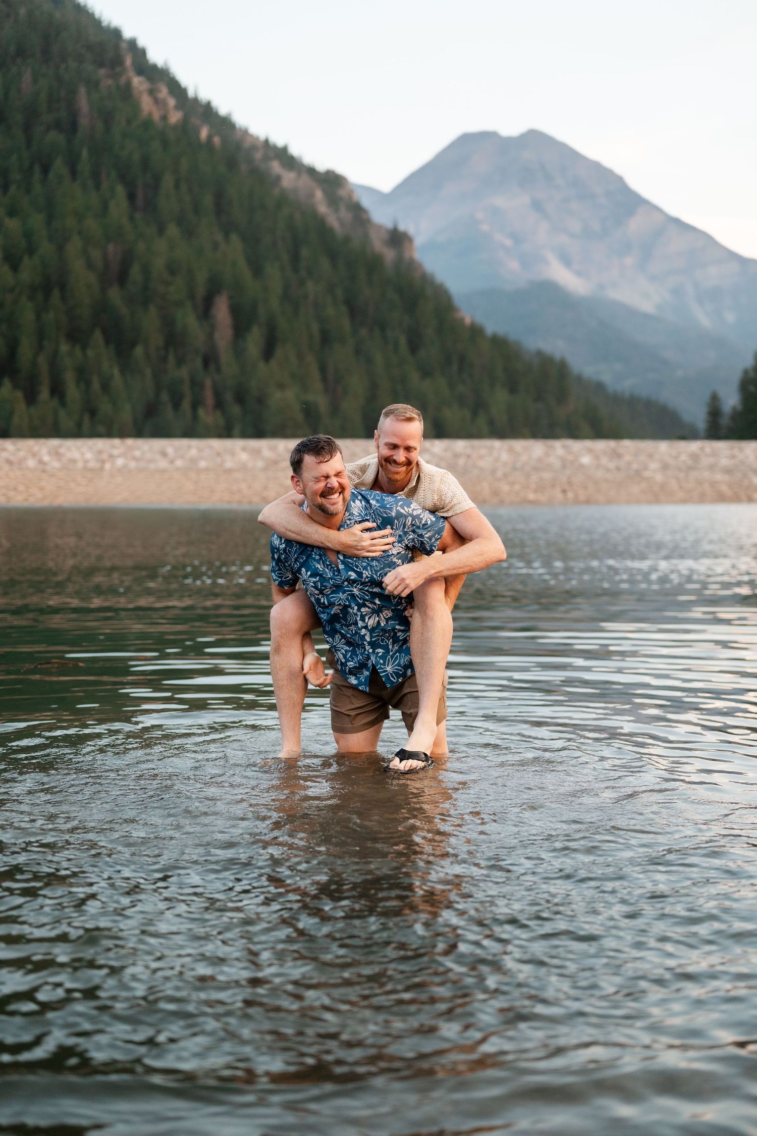 Couple having a water fight at Tibble Fork Reservoir. Two men laugh joyfully as one gives the other a piggyback ride in a mountain lake.