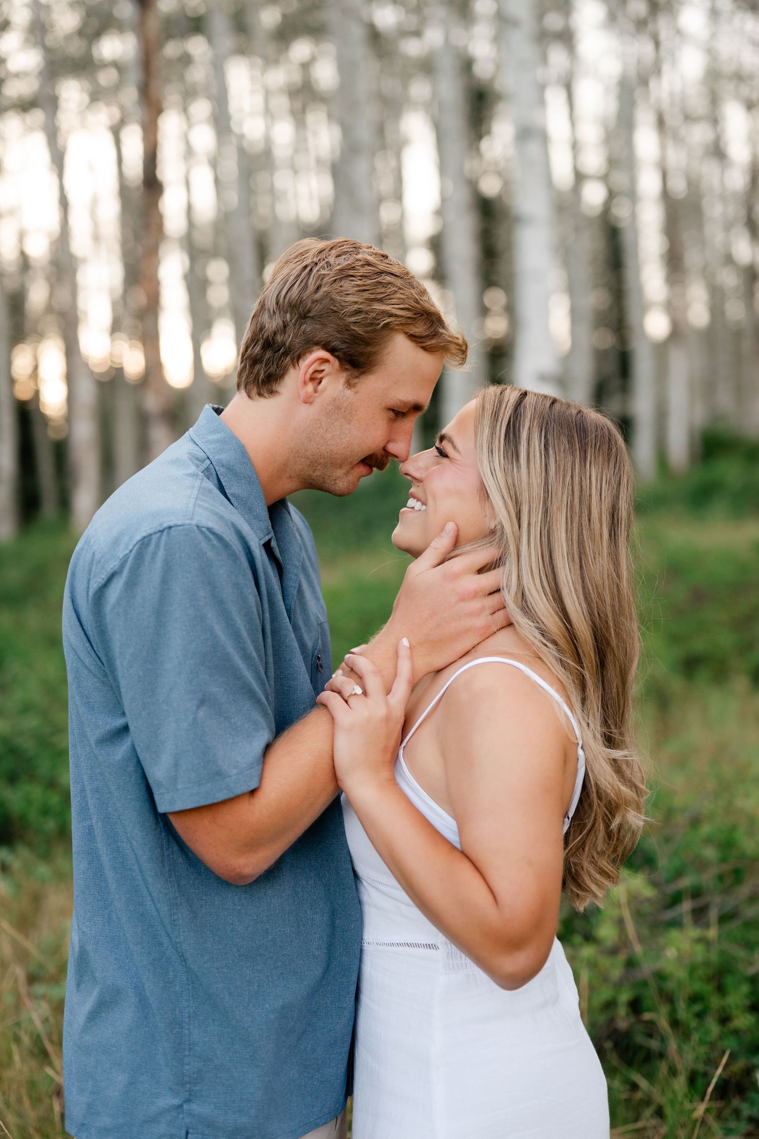 Couple sharing a romantic moment in an aspen forest touching foreheads. Romantic mountain engagement photos at guardsman pass.