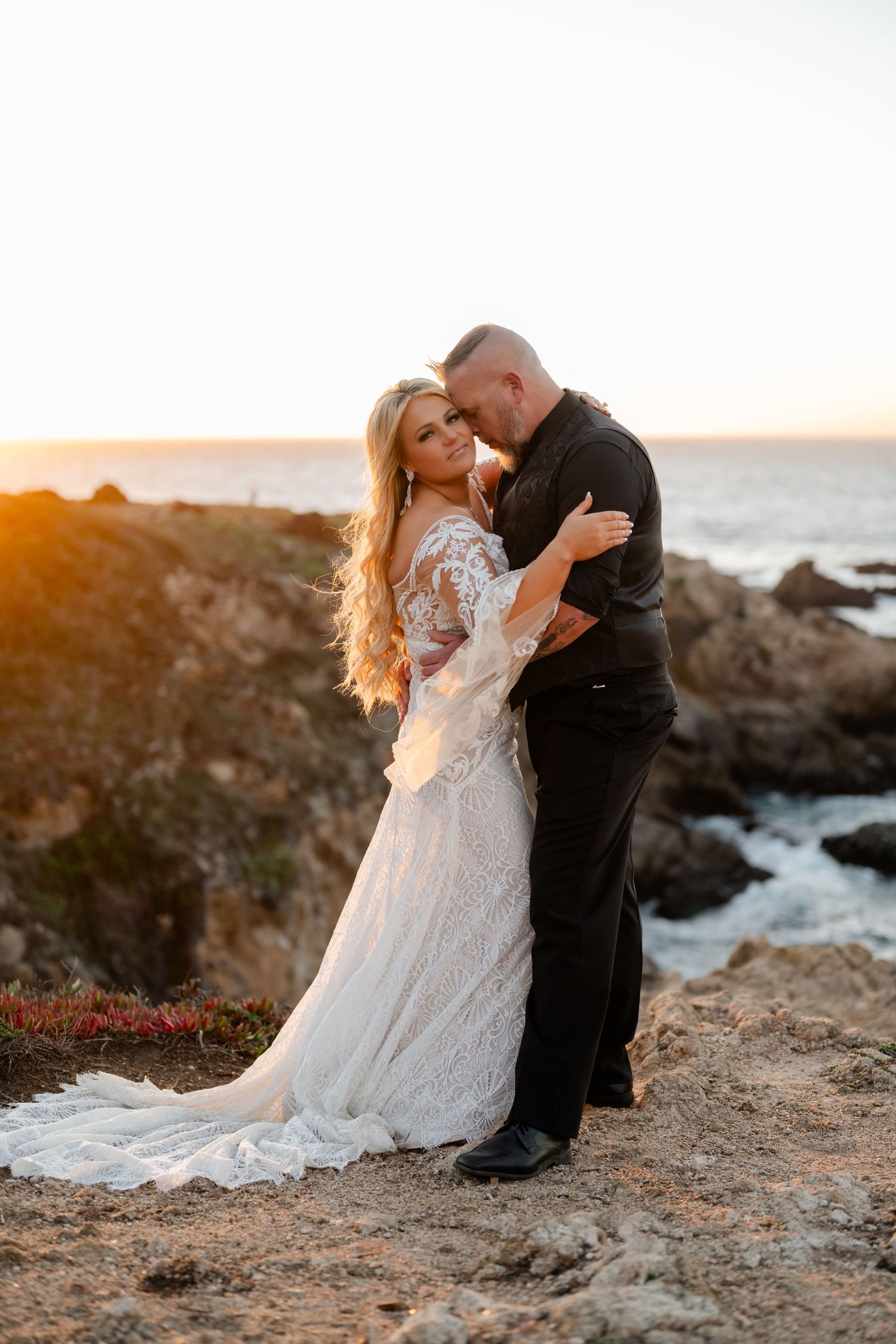Romantic sunset portrait of couple in wedding attire on rocky coastline.
