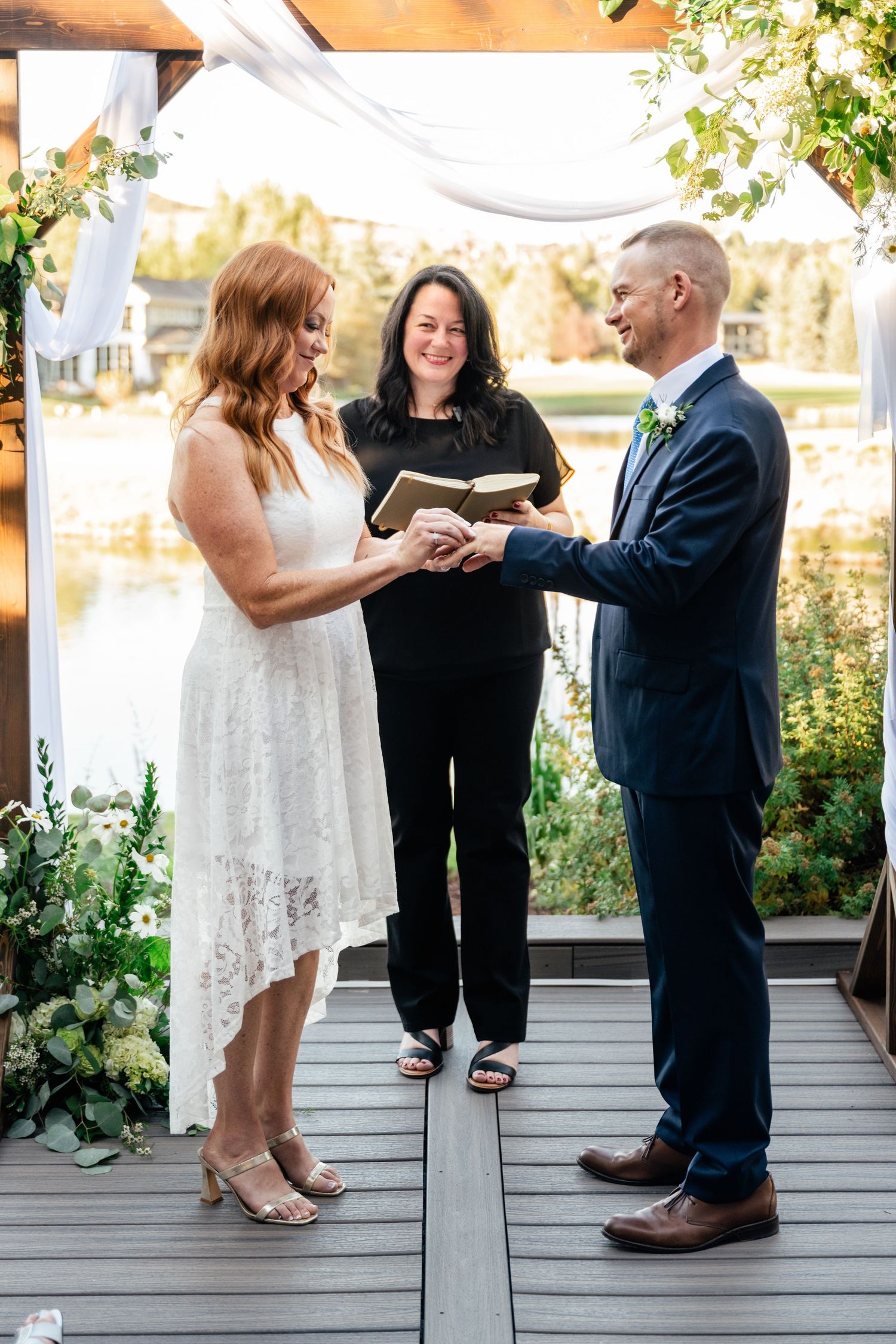 Wedding ring exchange ceremony on a lakeside deck during a beautiful autumn day.