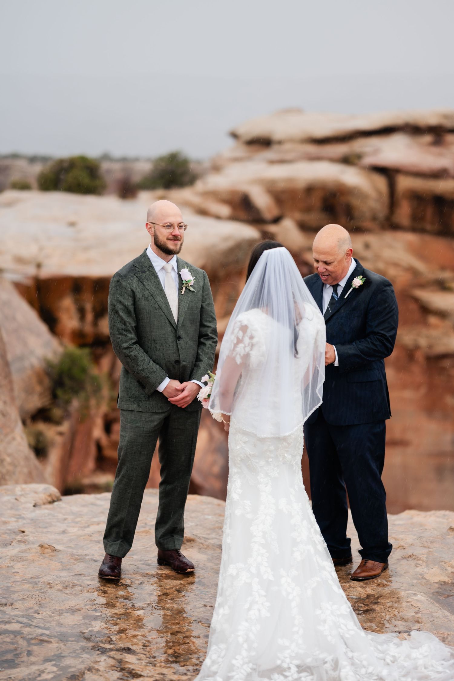 Wedding party gathered on rocky terrain in formal attire during outdoor ceremony.