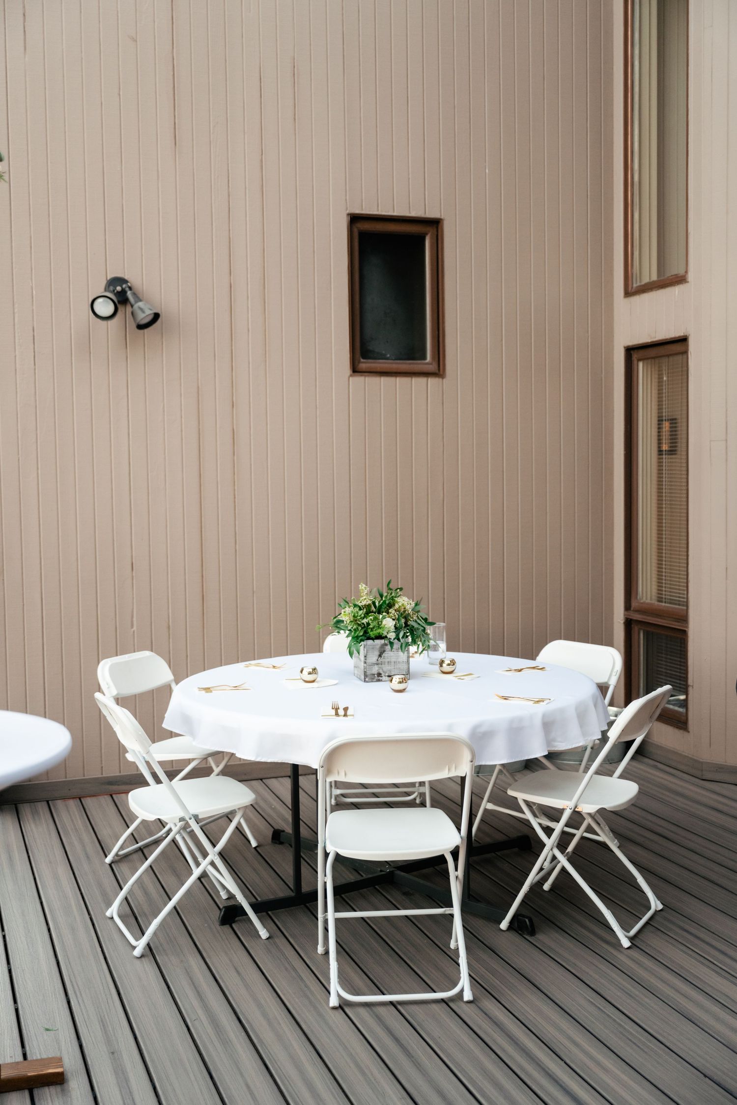 Outdoor patio setup with white folding chairs and round tables against a beige wall.