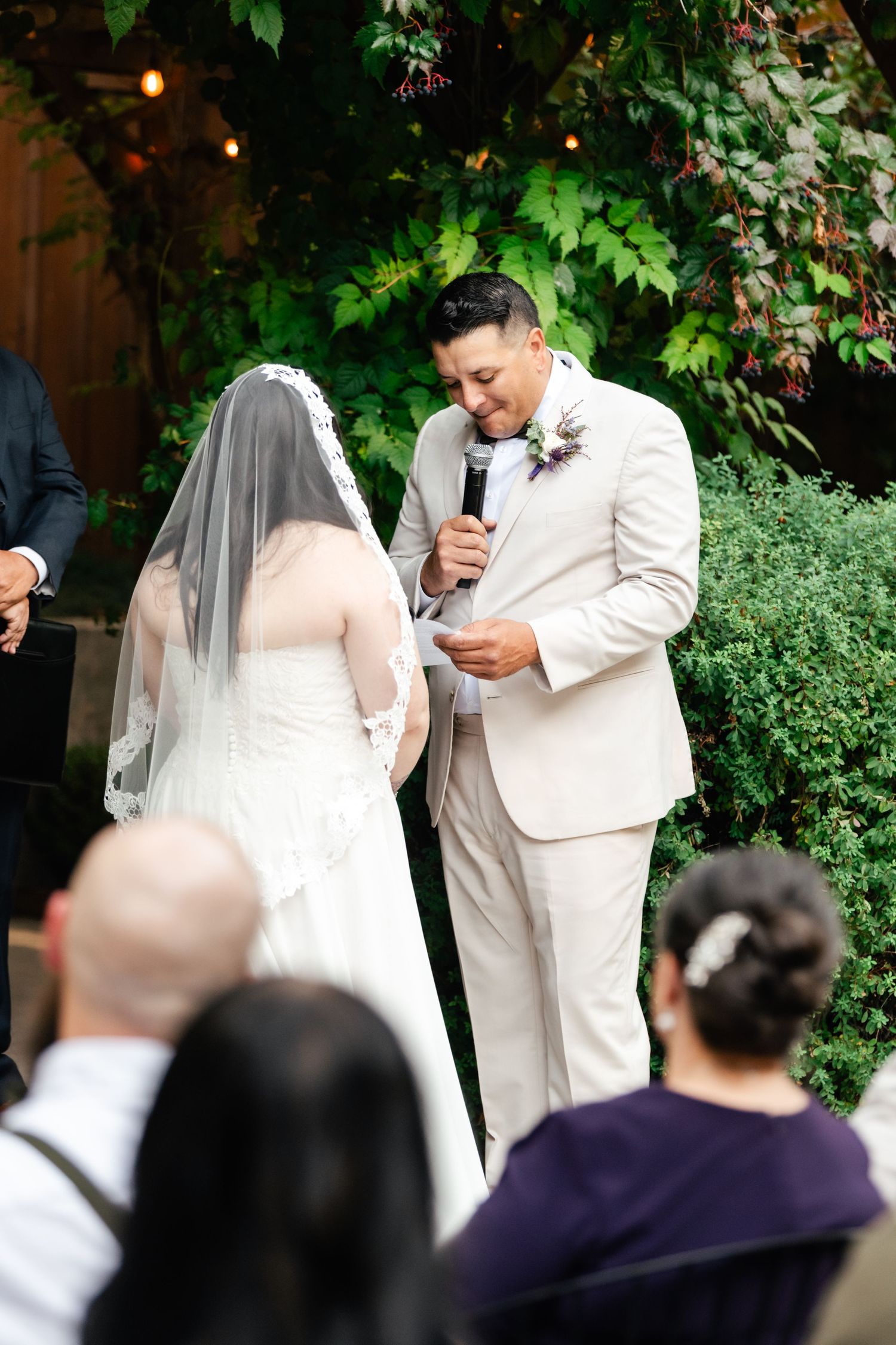 A couple exchanges vows during their wedding ceremony surrounded by lush greenery and guests.