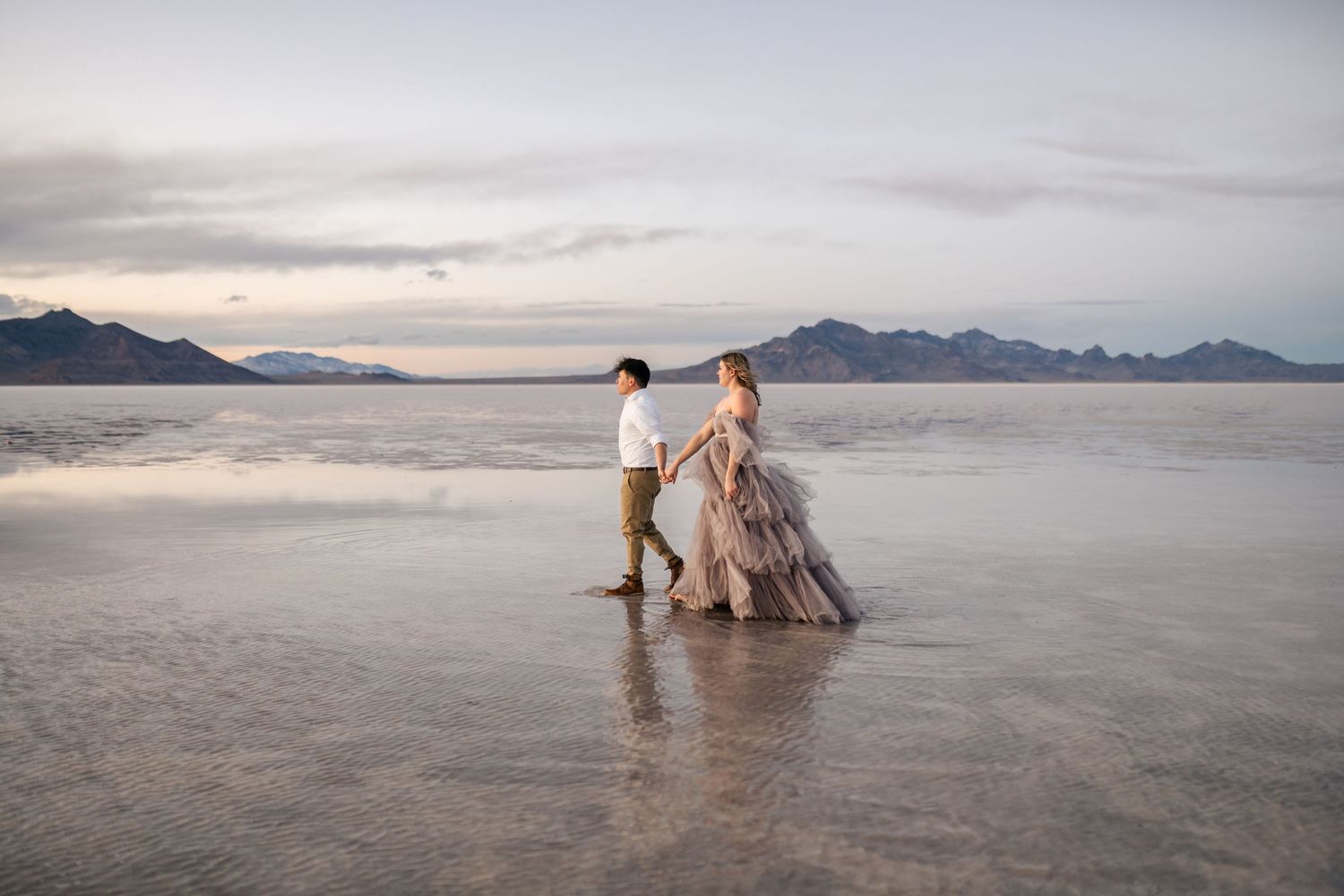 A couple walks together during blue hour of a couple's photo session at the flooded Salt Flats.