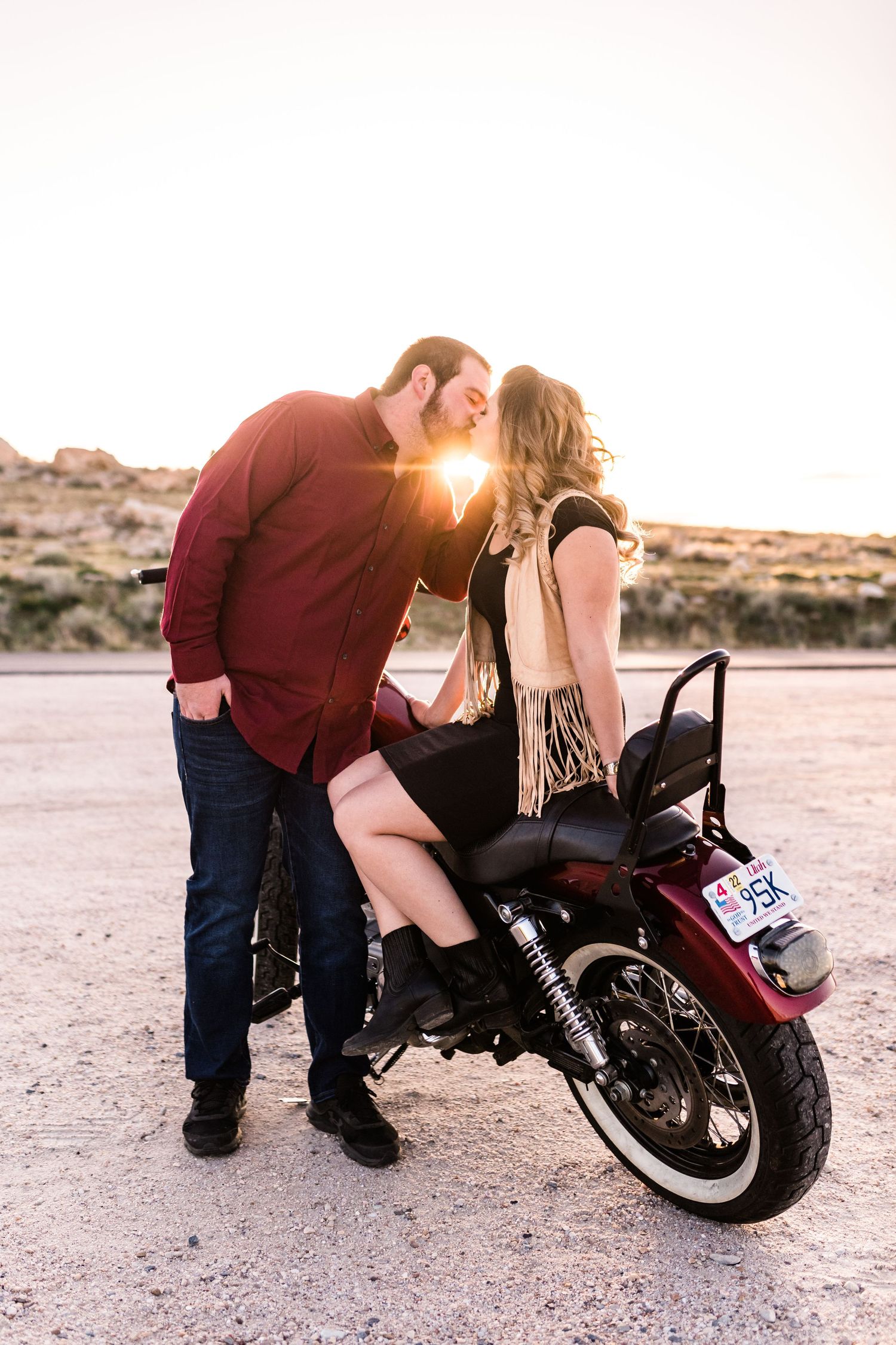 A couple shares a romantic moment near a motorcycle at sunset in the desert.