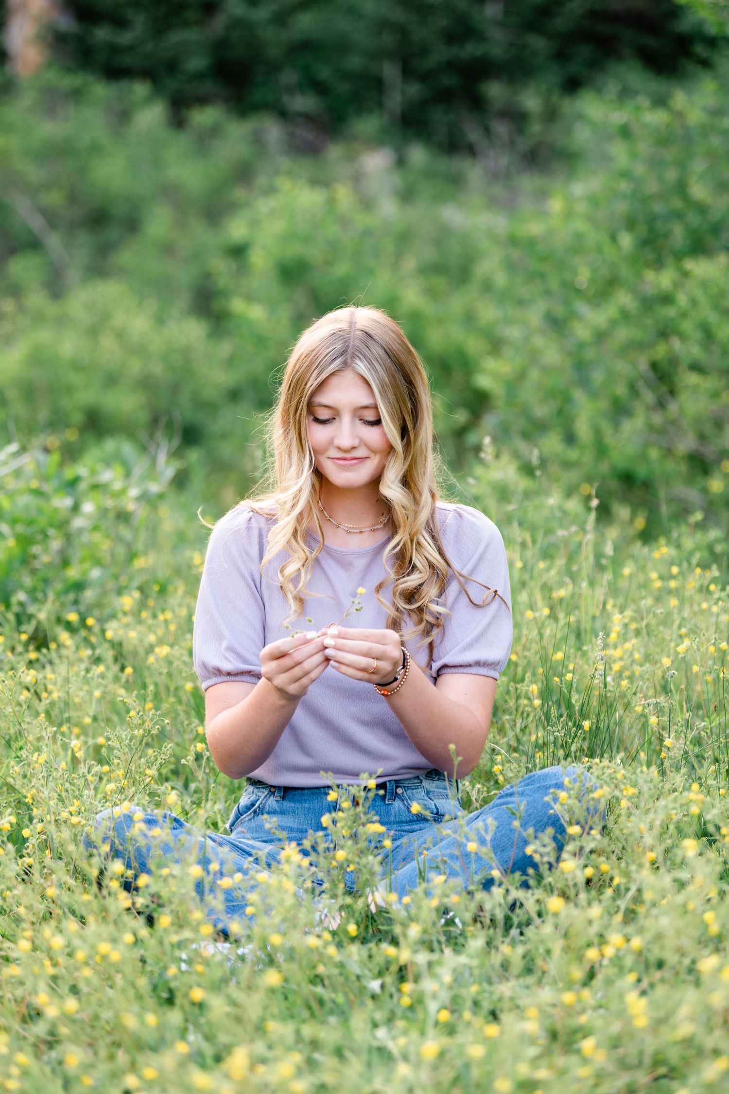A person in a white t-shirt and jeans sits in a sunny meadow filled with yellow wildflowers.