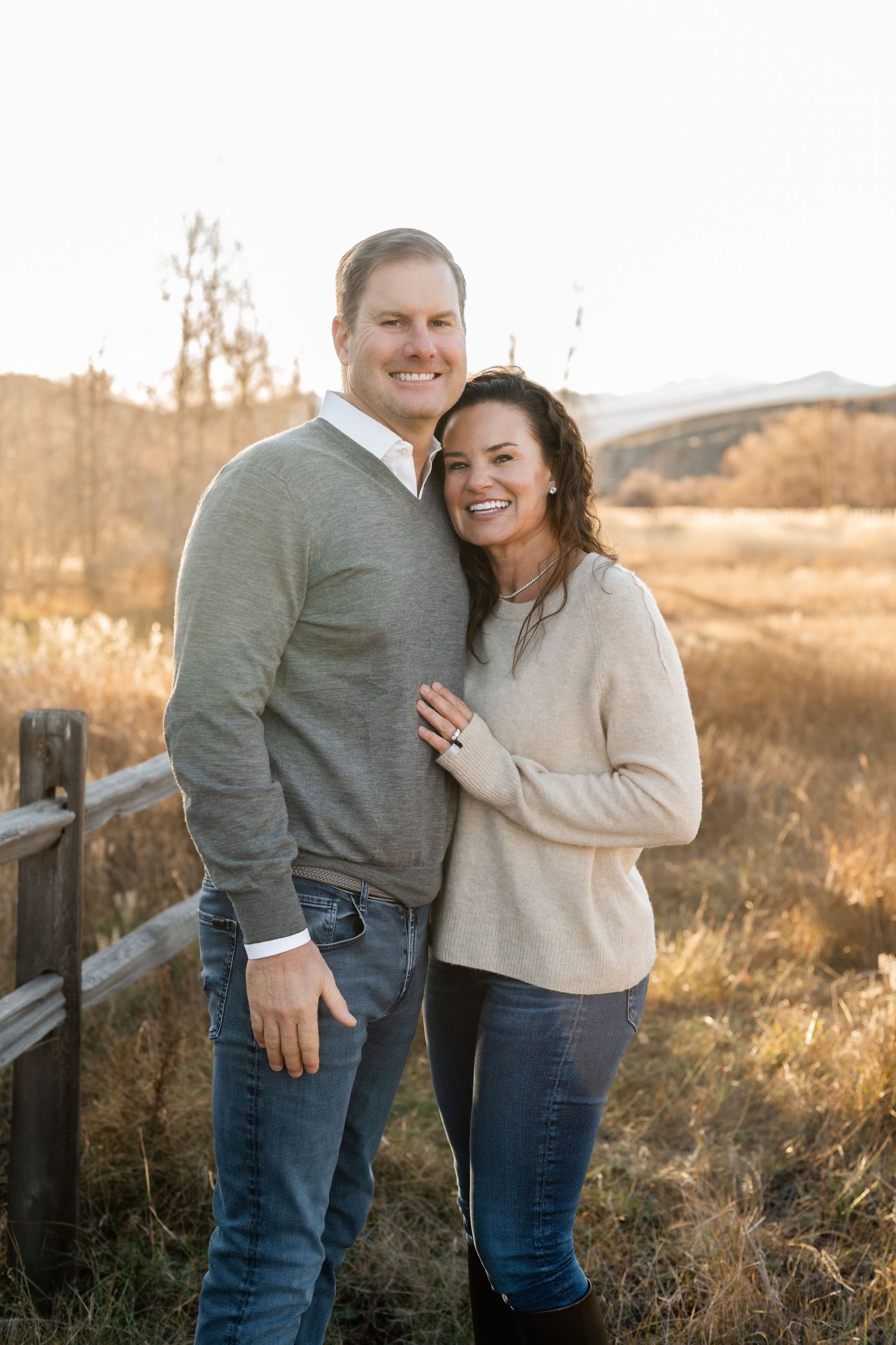 Couple shares intimate moments along a rustic wooden fence during golden hour sunset in a rural field setting.