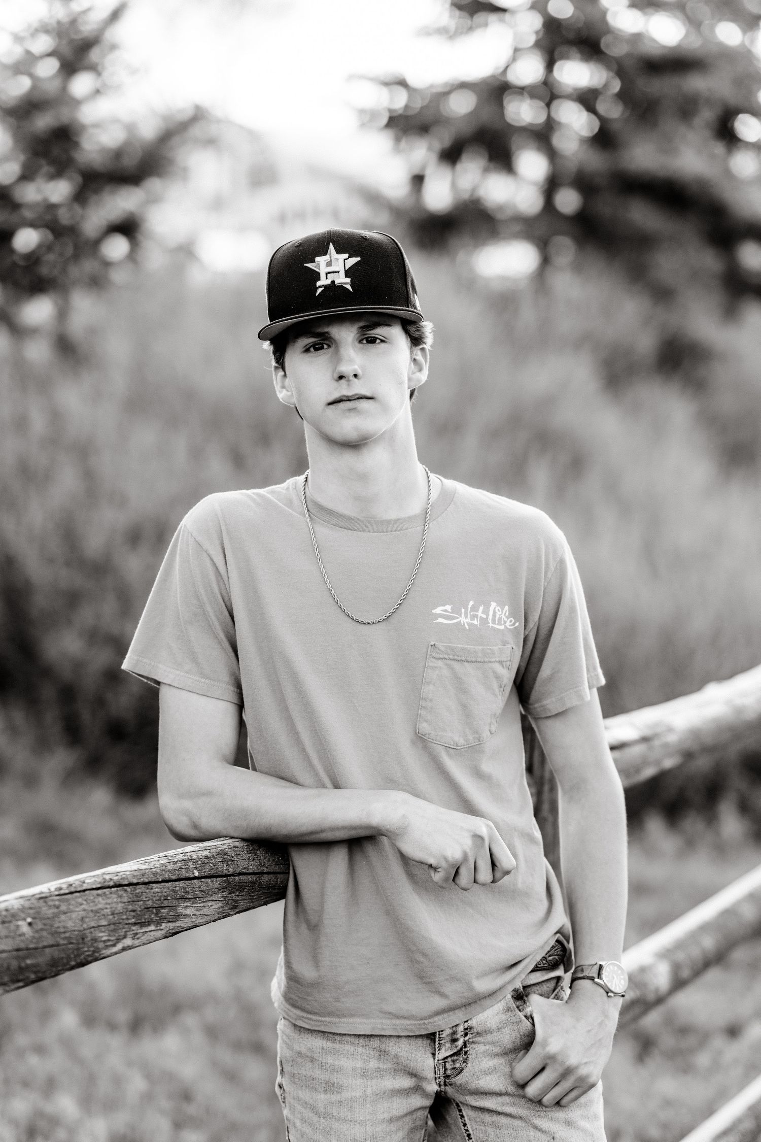 A black and white photo series shows someone in a baseball cap and t-shirt leaning against a wooden railing outdoors.