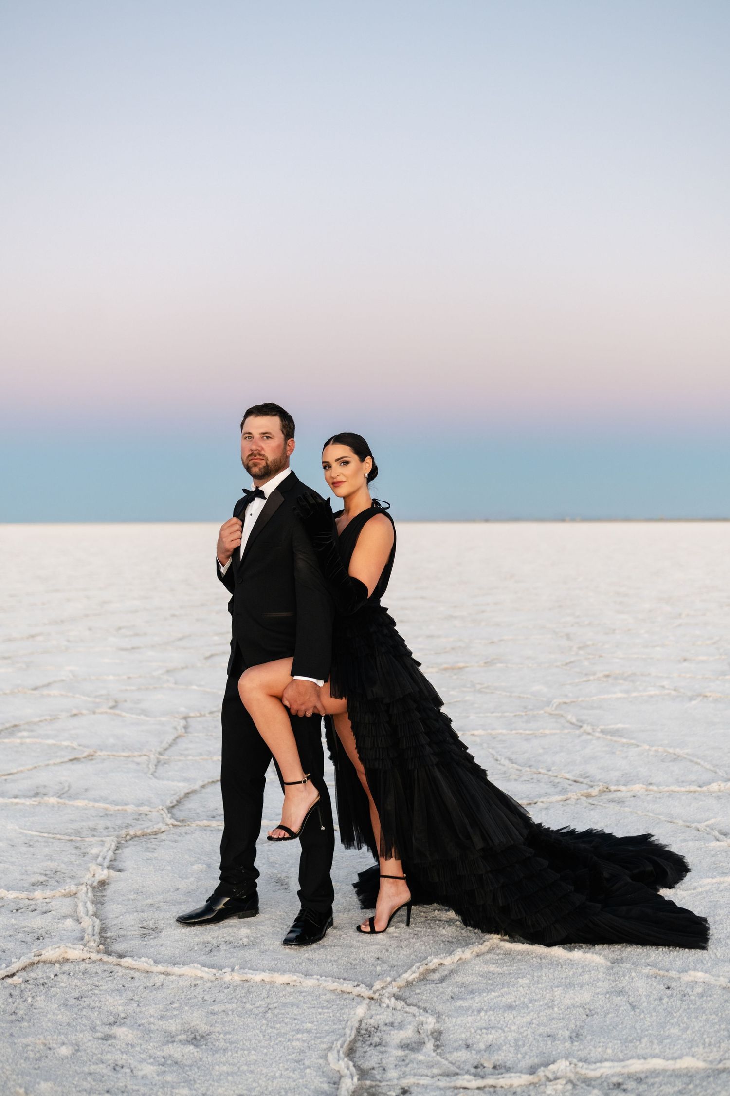 Utah Salt Flats Photographer. A couple in formal black attire poses intimately on white salt flats during golden hour.