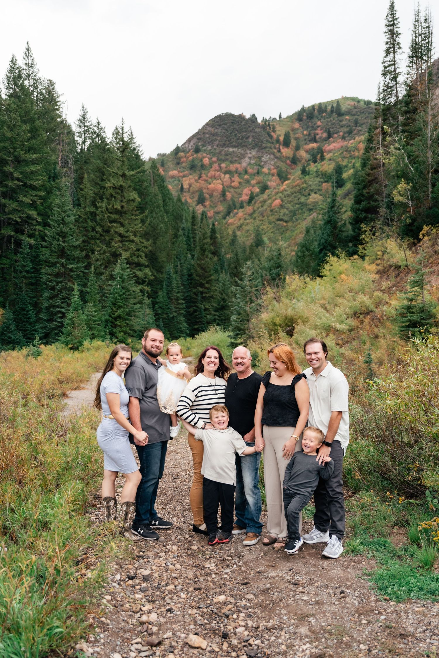 A group stands together on a mountain trail surrounded by evergreen trees and autumn foliage in the wilderness.