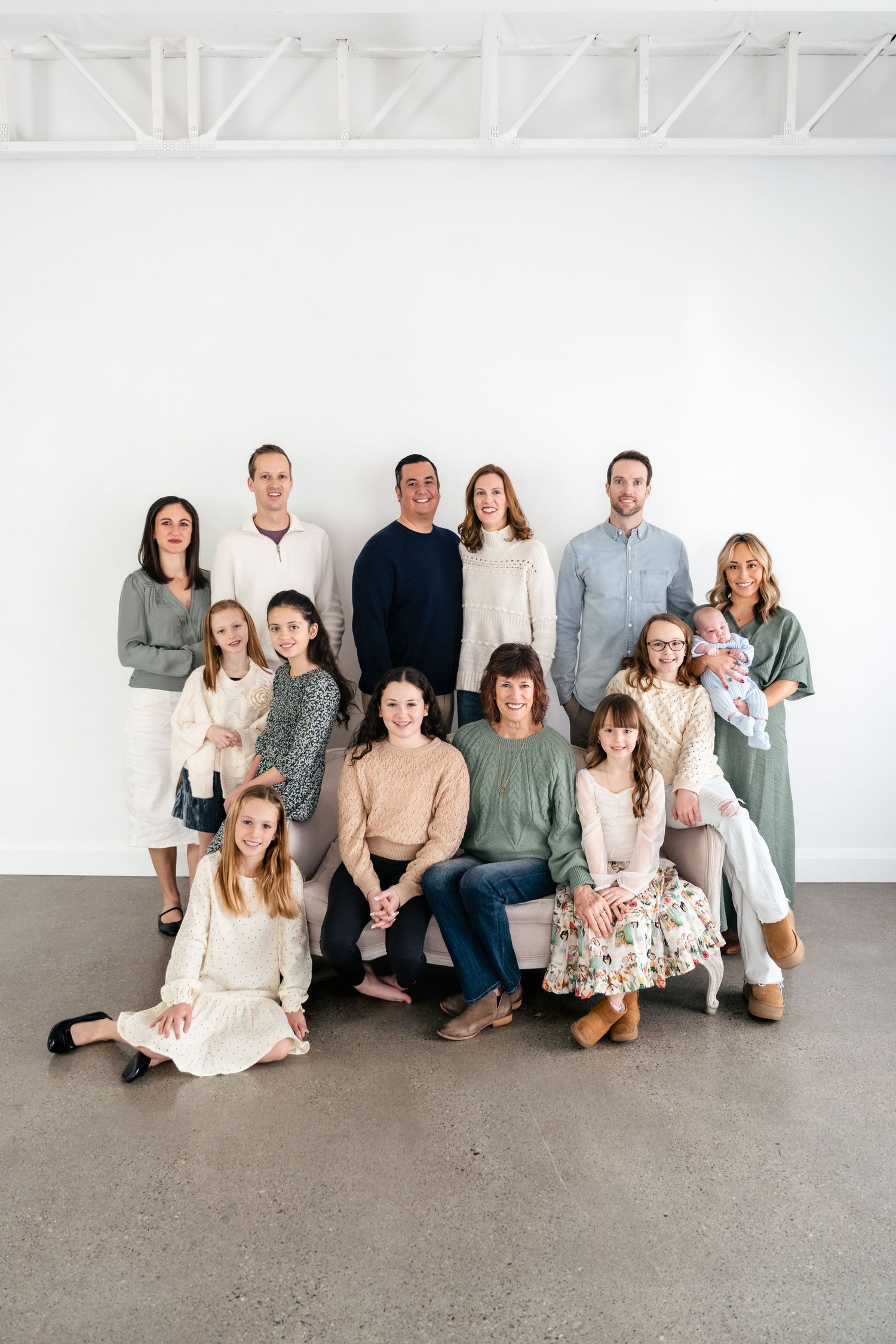 Professional family portrait series showing a group in coordinated neutral outfits sitting and standing against a white wall.